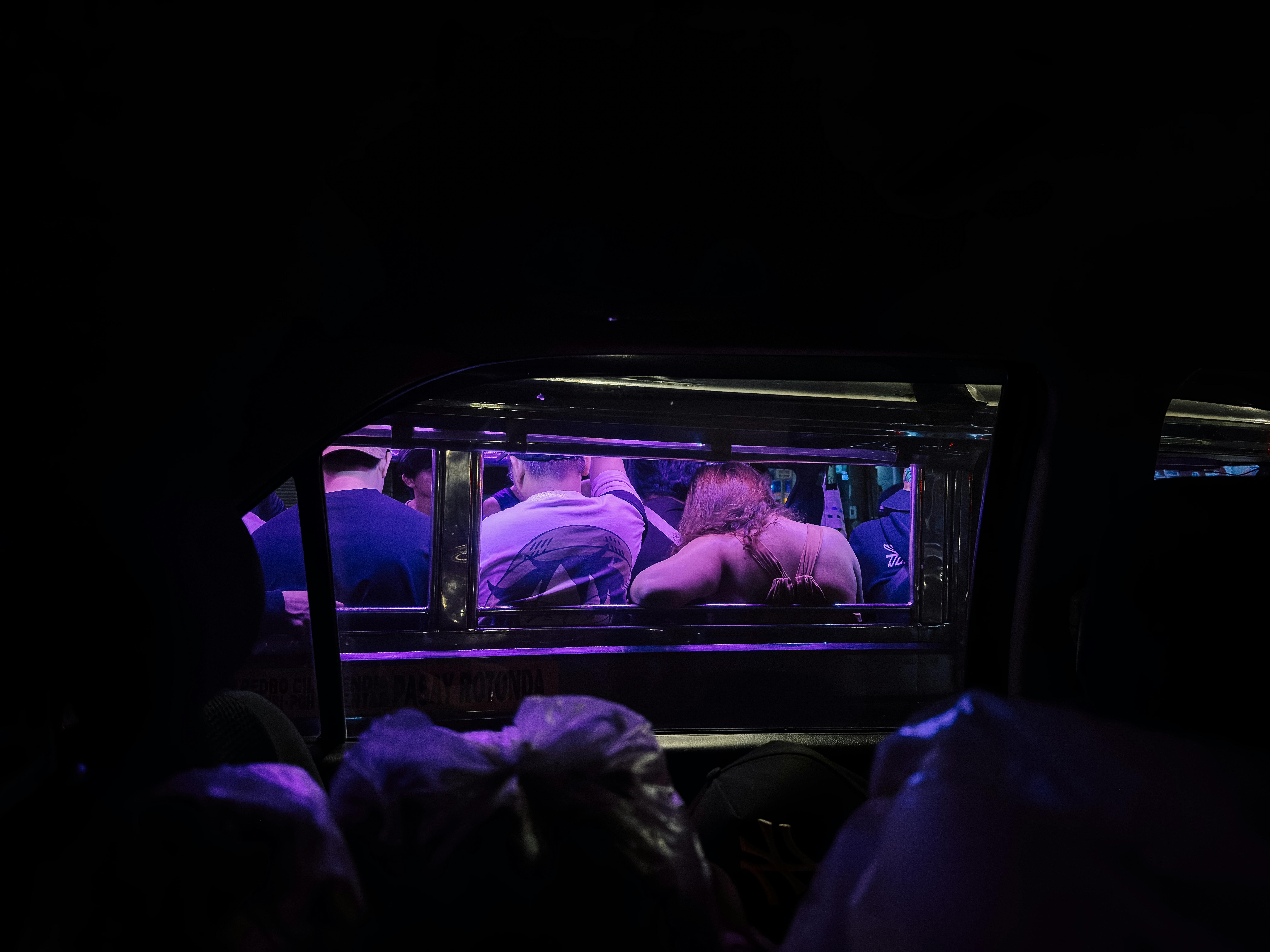 Free Passengers enjoy the vibrant purple lighting inside a jeepney at night, capturing urban nightlife. Stock Photo