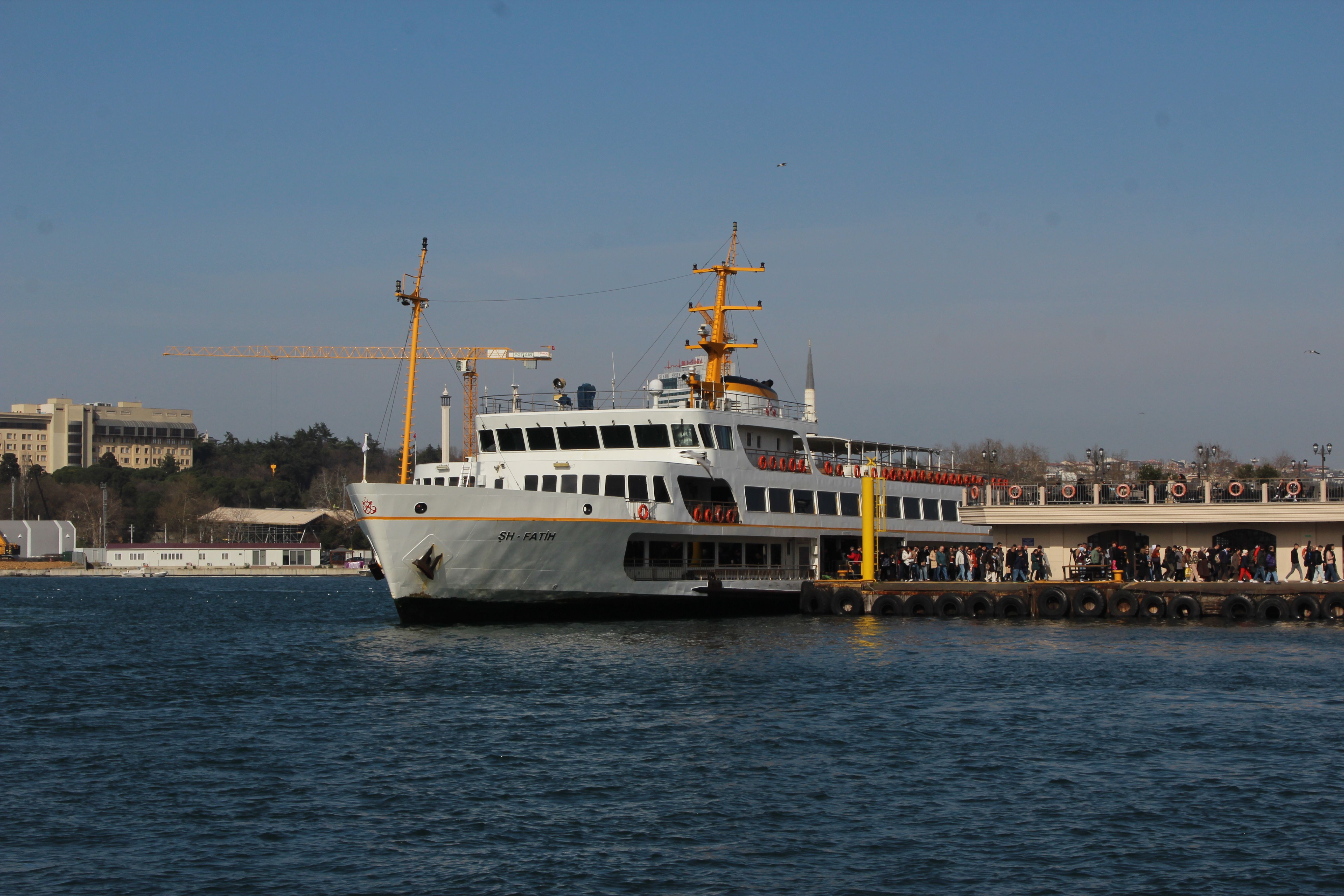 A ferry with people boarding at a busy port in Istanbul, viewed in daytime.