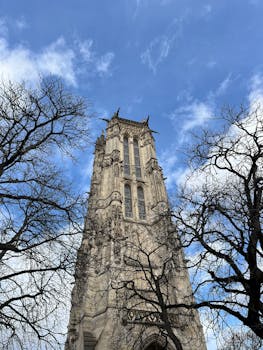 Majestic view of Saint-Jacques Tower in Paris framed by leafless trees against a blue sky.