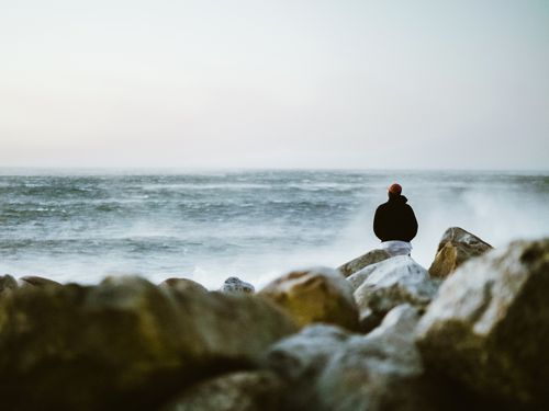Free A lone person stands on a rocky shore facing the ocean in Cape Town, South Africa. Stock Photo