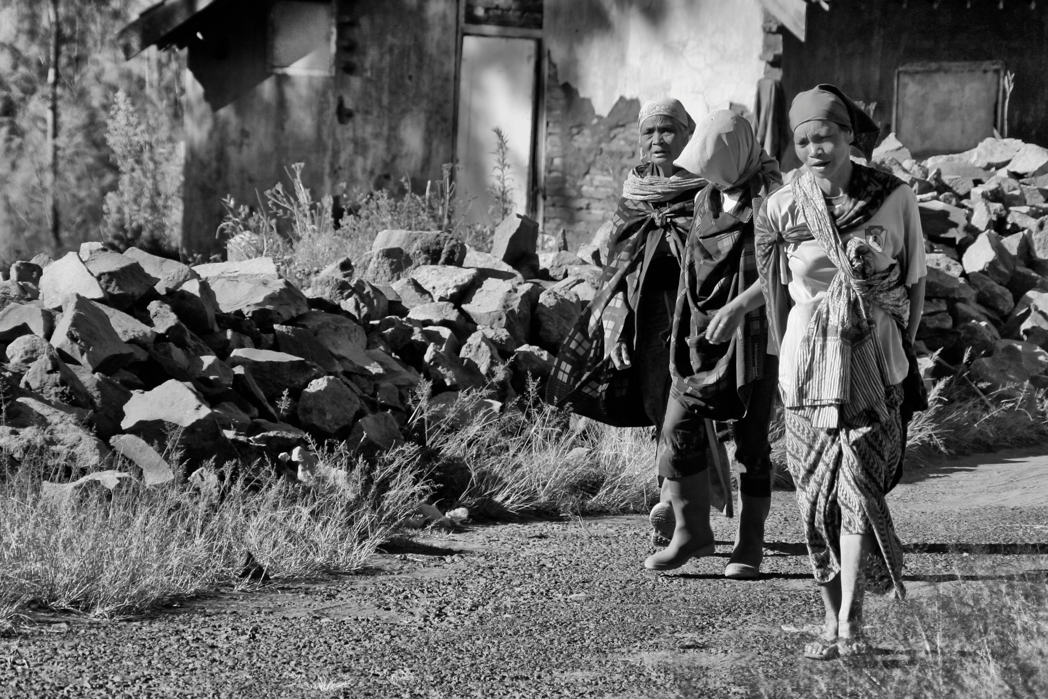 Kostenlos Schwarz-Weiß-Foto von drei Personen, die an einem verfallenen Gebäude und Steinhaufen vorbeigehen. Stock-Foto