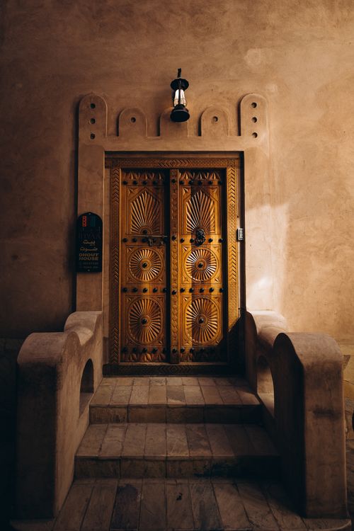 Free Capture of a beautifully carved traditional wooden door in Oman, highlighted by a vintage lantern. Stock Photo
