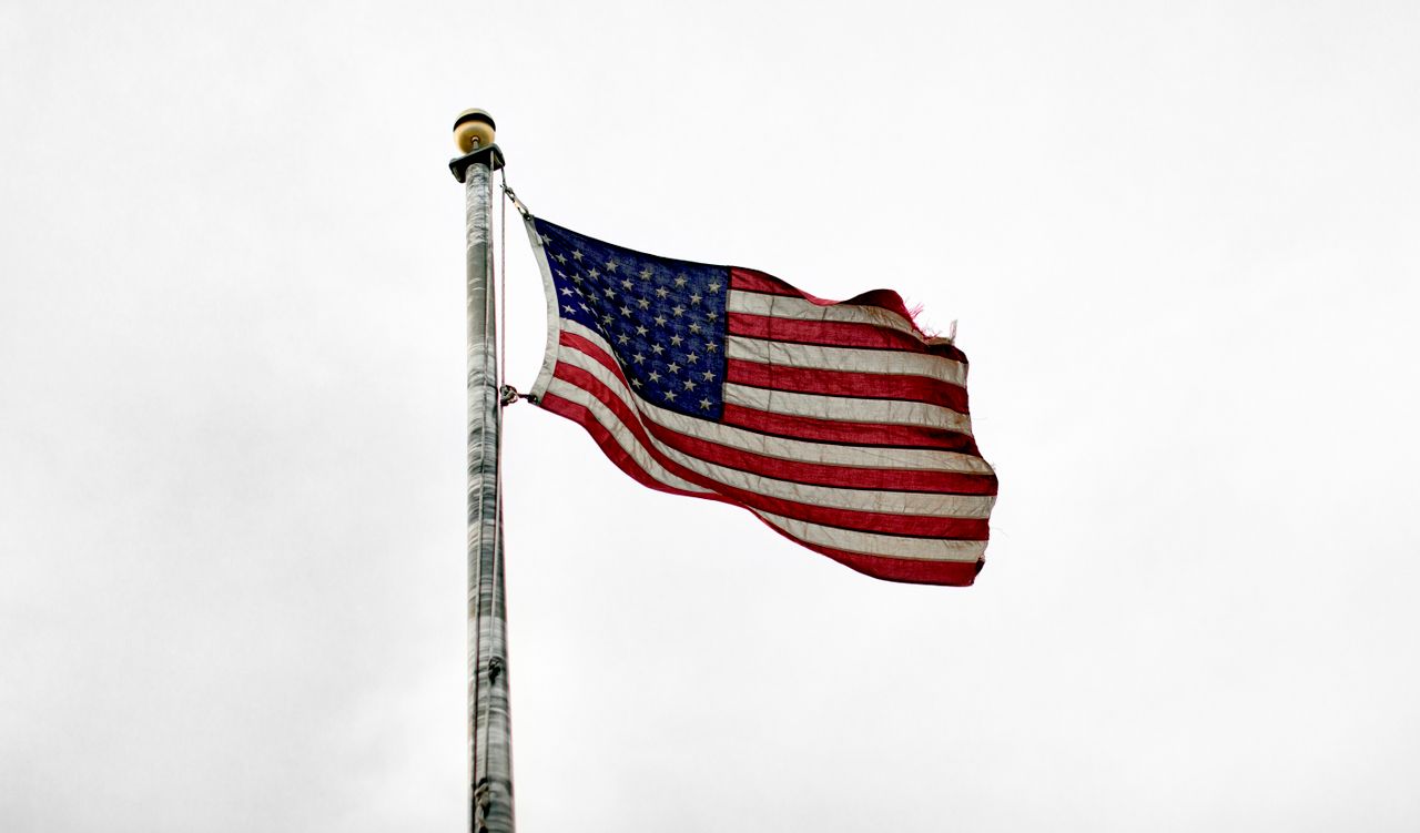 united states flag on a flagpole billowing against a cloudy sky symbol