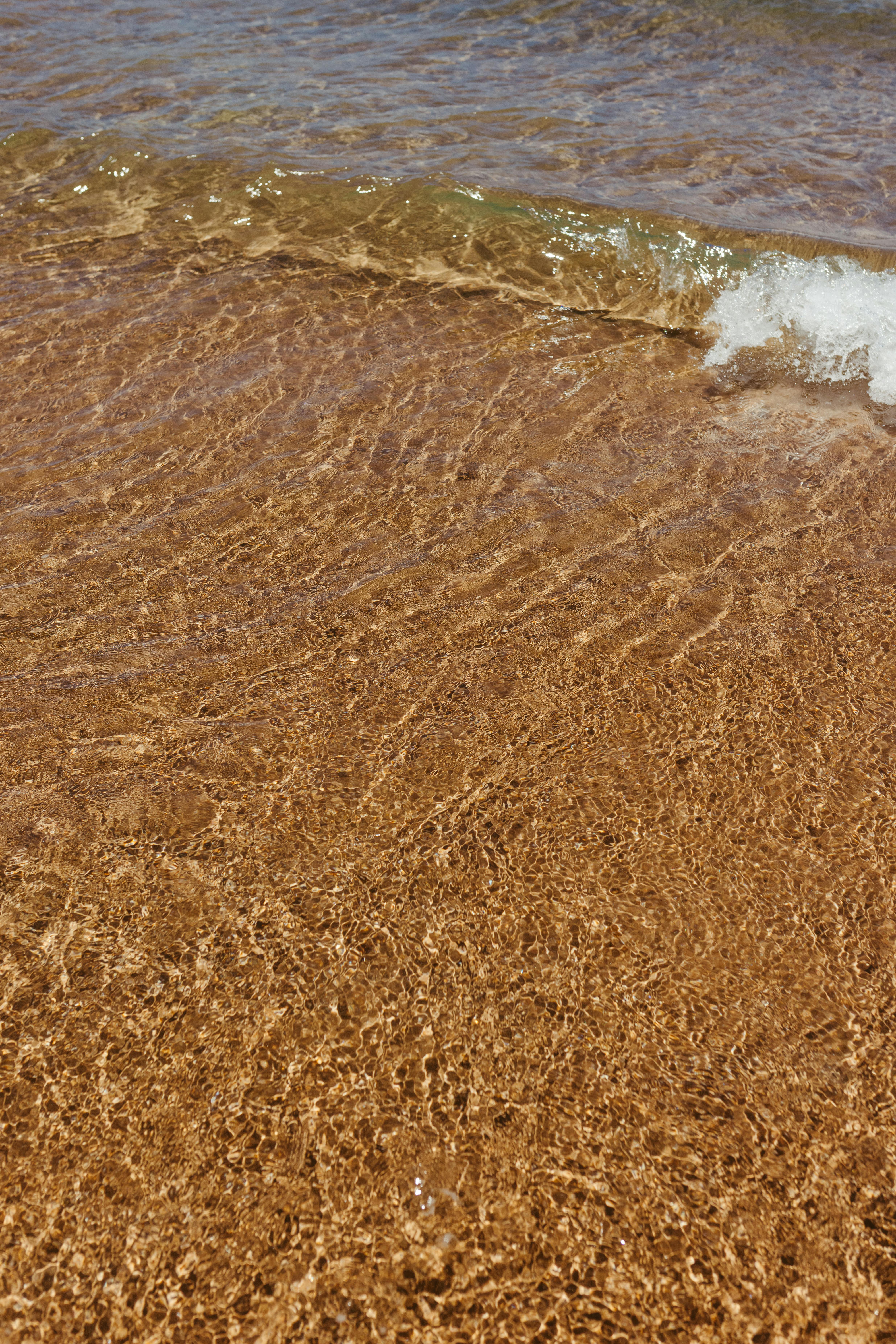 Kostenlos Eine sanfte Welle umspült einen strukturierten Sandstrand und fängt die Essenz sommerlicher Ruhe ein. Stock-Foto
