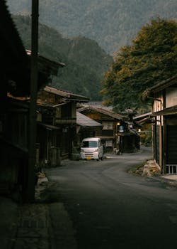 Serene street view in a traditional Japanese village with wooden houses and mountains.