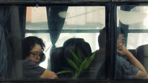 Two people sit inside a bus, viewed through a window, exuding a contemplative mood.