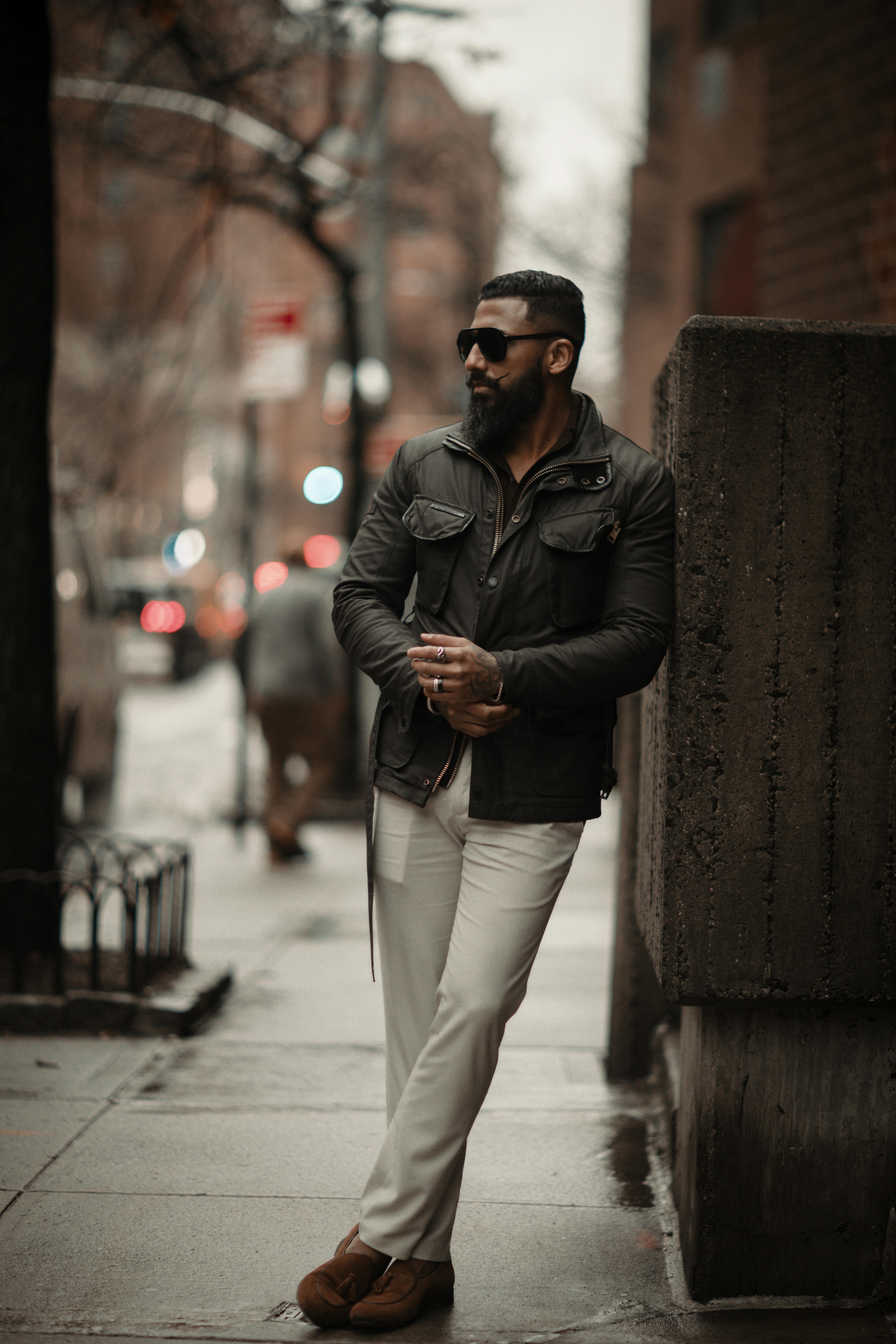 Kostenlos Ein modisch gekleideter Mann lehnt an einer Mauer in einer Stadtstraße und verkörpert den modernen urbanen Lebensstil. Stock-Foto