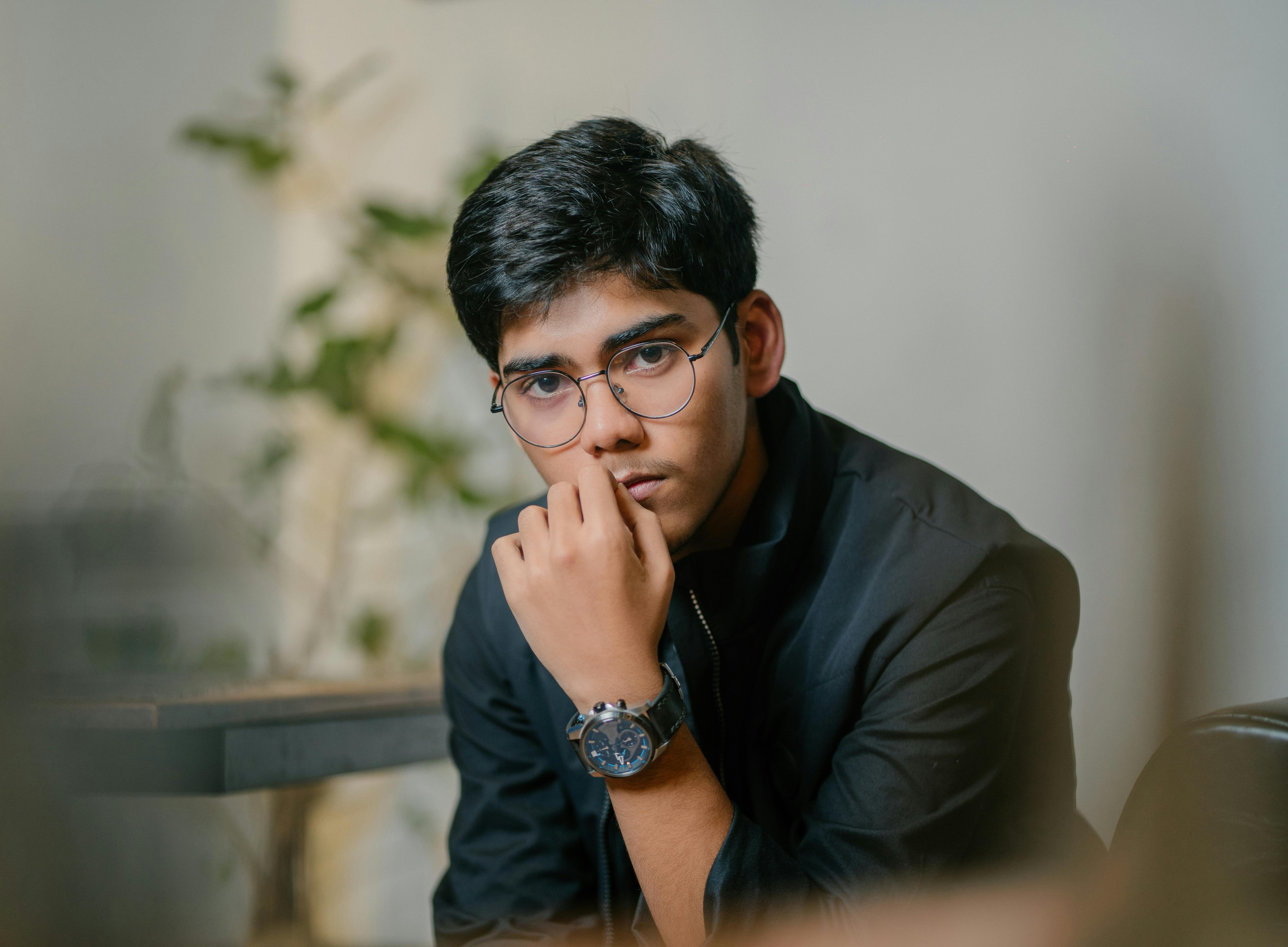 Kostenlos Porträt eines jungen Mannes mit Brille in nachdenklicher Pose, in einem Innenraum. Stock-Foto