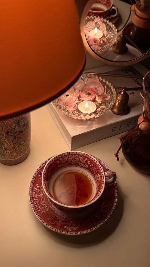 Free Cozy evening setup with a floral teacup, candle, and warm lighting creating a relaxing ambiance. Stock Photo