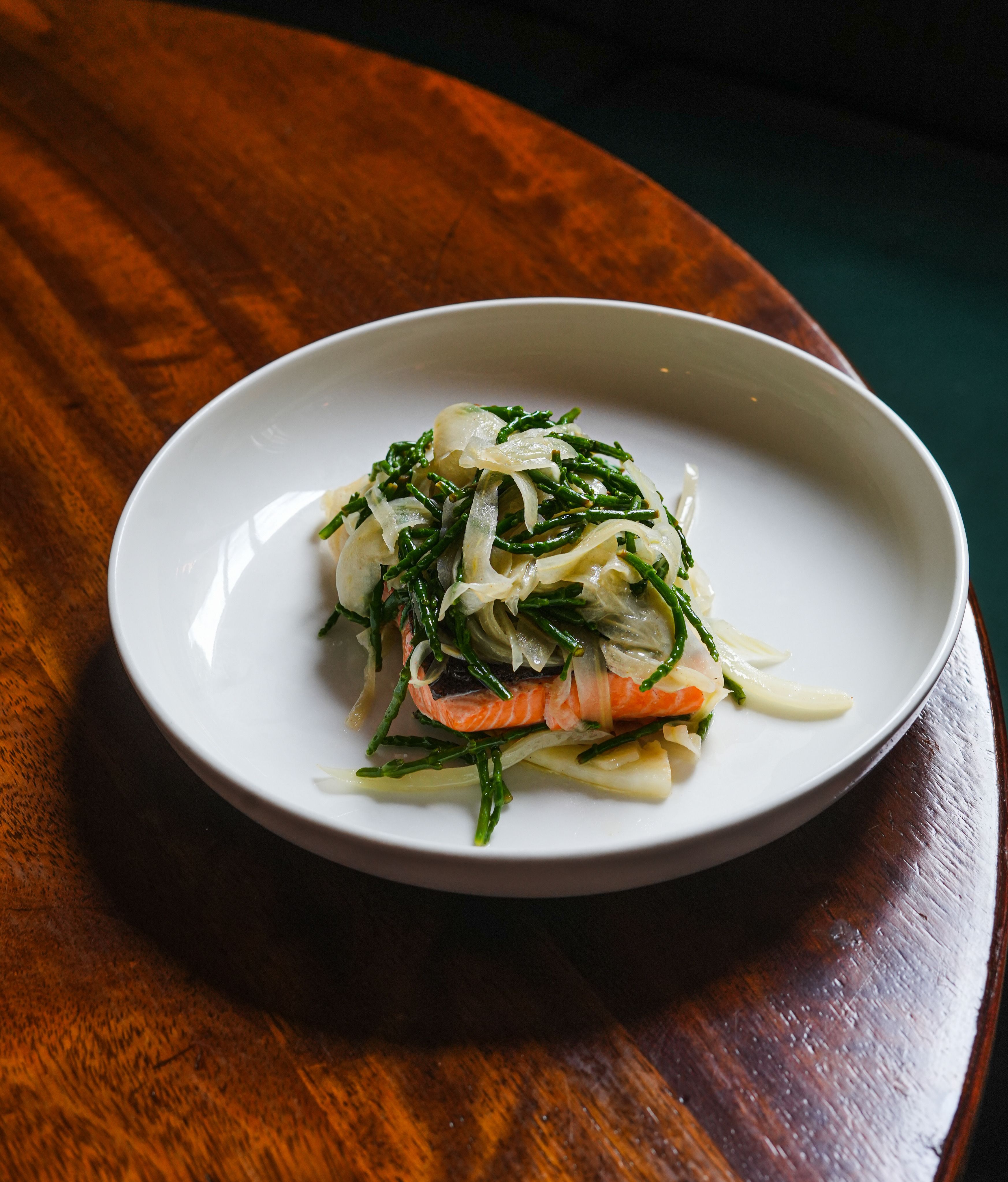 A mouthwatering salmon fillet dish garnished with fresh greens on a wooden table.