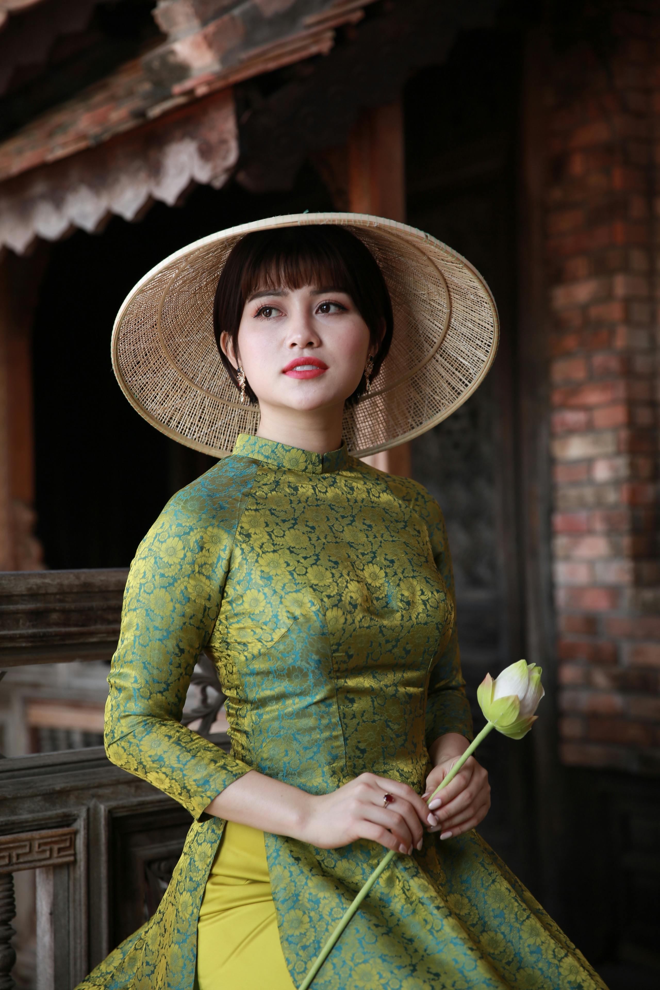 一位戴着草帽、穿着传统服装的女人，手拿一朵花，神情泰然