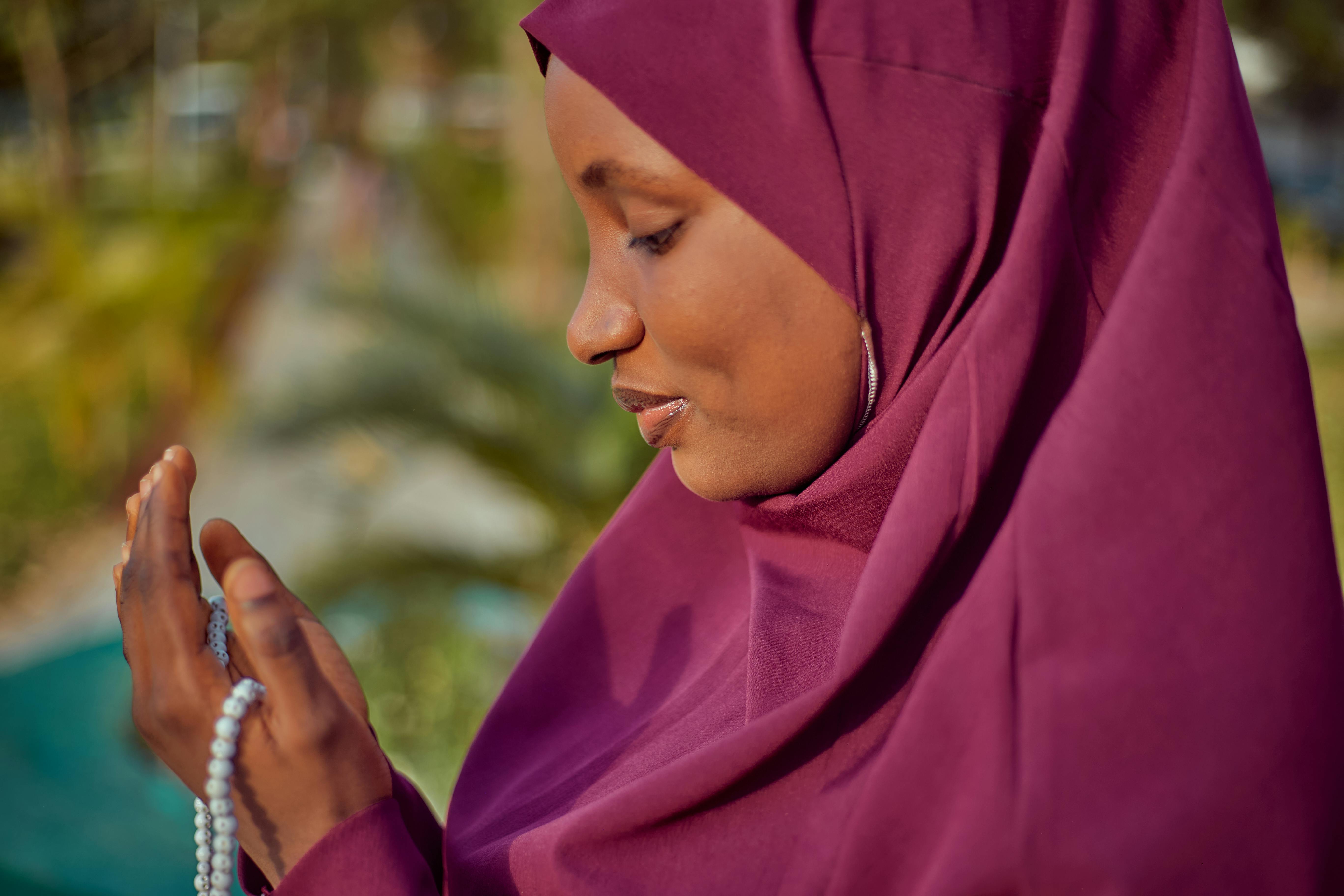 Kostenlos Eine Frau mit violettem Hidschab betet im Freien mit einem Rosenkranz in der Hand. Stock-Foto