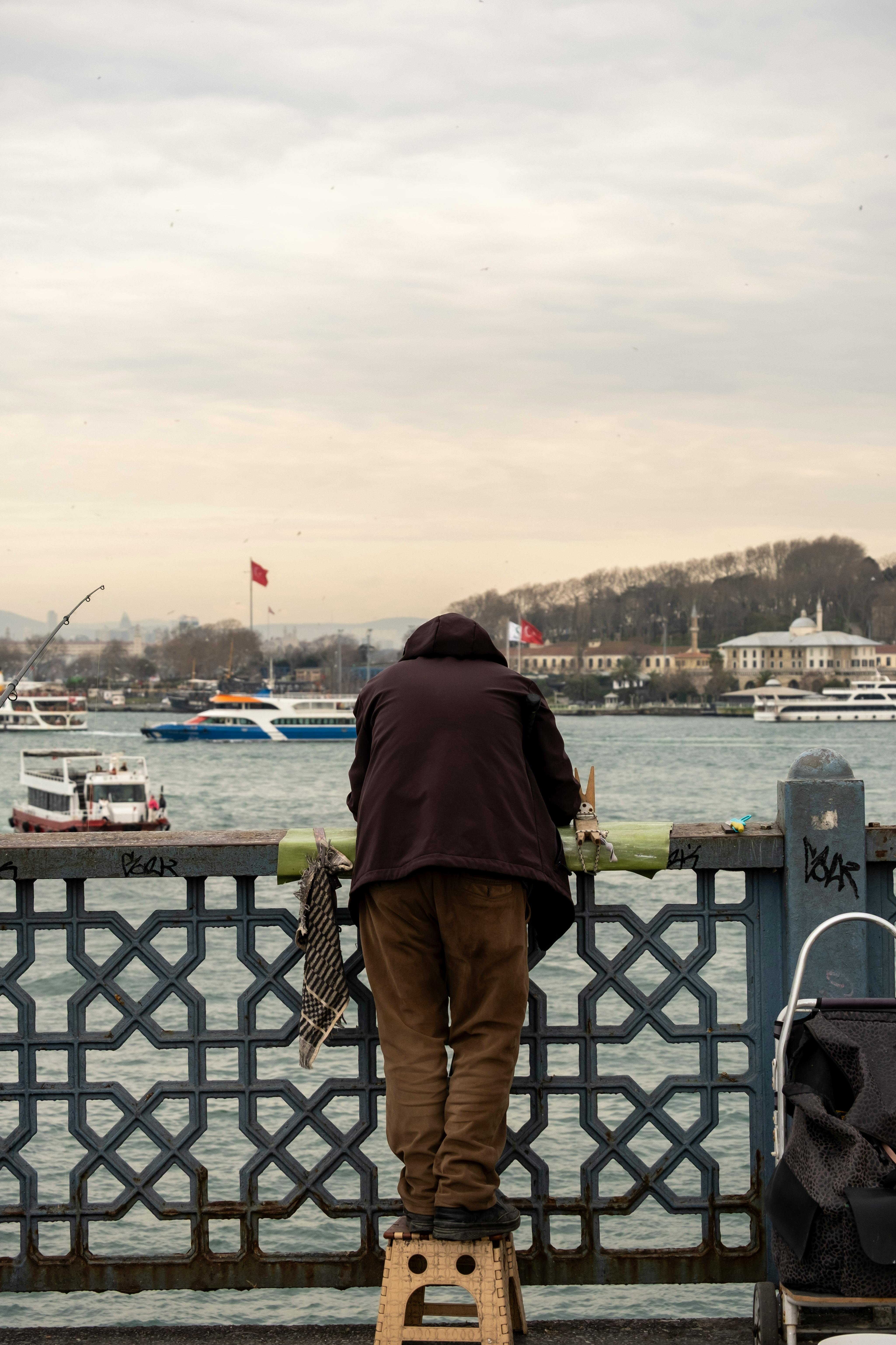 Kostenlos Ein Mann angelt auf der berühmten Galatabrücke in Istanbul und überblickt die belebte Wasserstraße mit ihren Booten. Stock-Foto