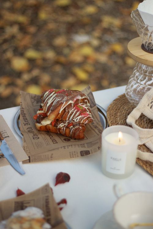 Free A cozy autumn picnic scene featuring a croissant with icing and a lit candle on a table. Stock Photo