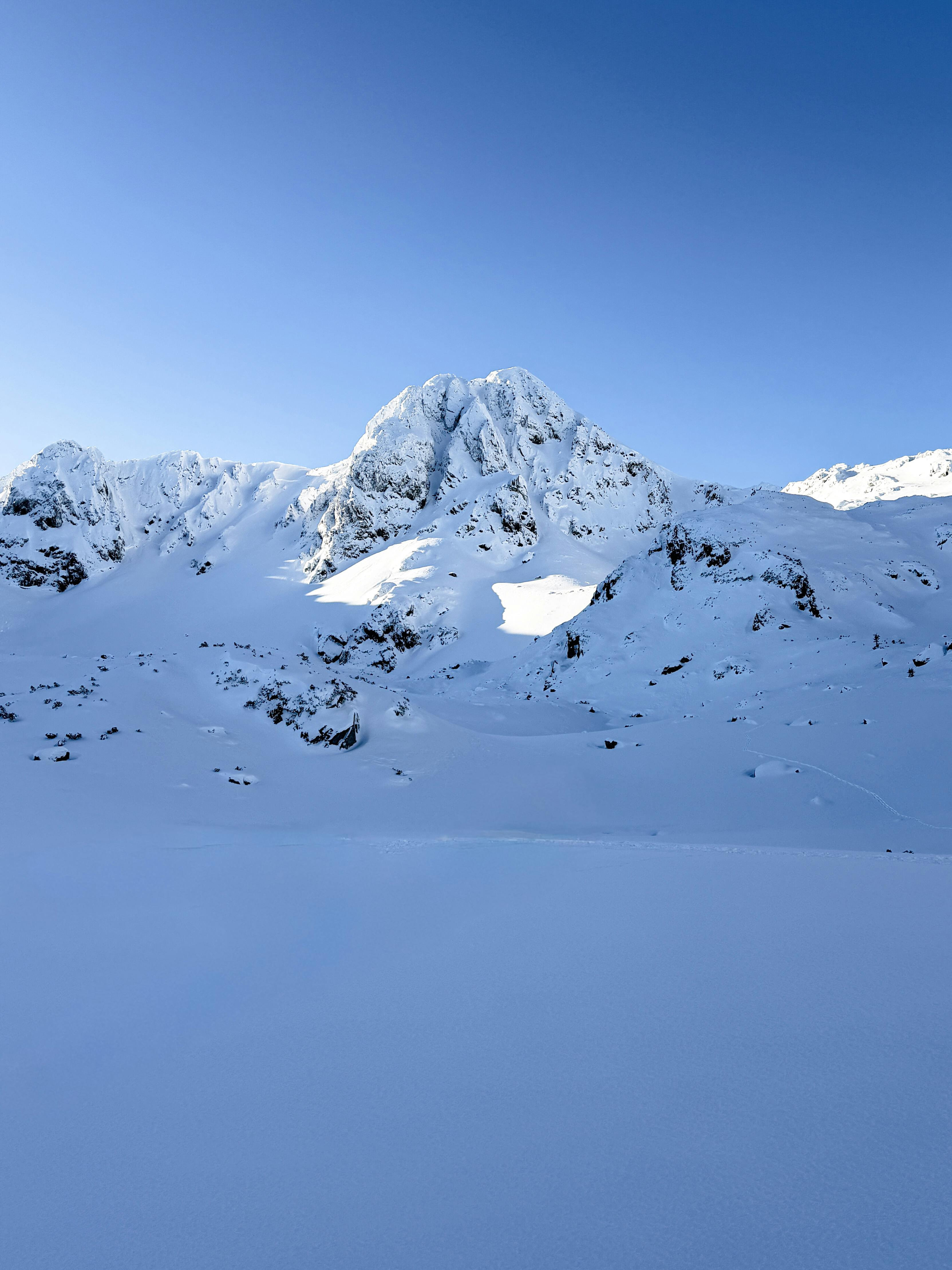 Δωρεάν Μια γαλήνια θέα στα παρθένα χιονισμένα βουνά κάτω από έναν λαμπερό γαλάζιο ουρανό, που αναδεικνύει την ομορφιά του χειμώνα. Φωτογραφία από στοκ φωτογραφιών
