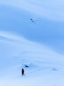A lone hiker in a red jacket traverses a vast, snowy expanse, capturing the essence of winter solitude and exploration.