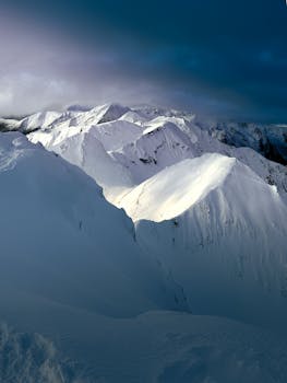 Sunlit snowy peaks under moody skies create a breathtaking alpine vista.