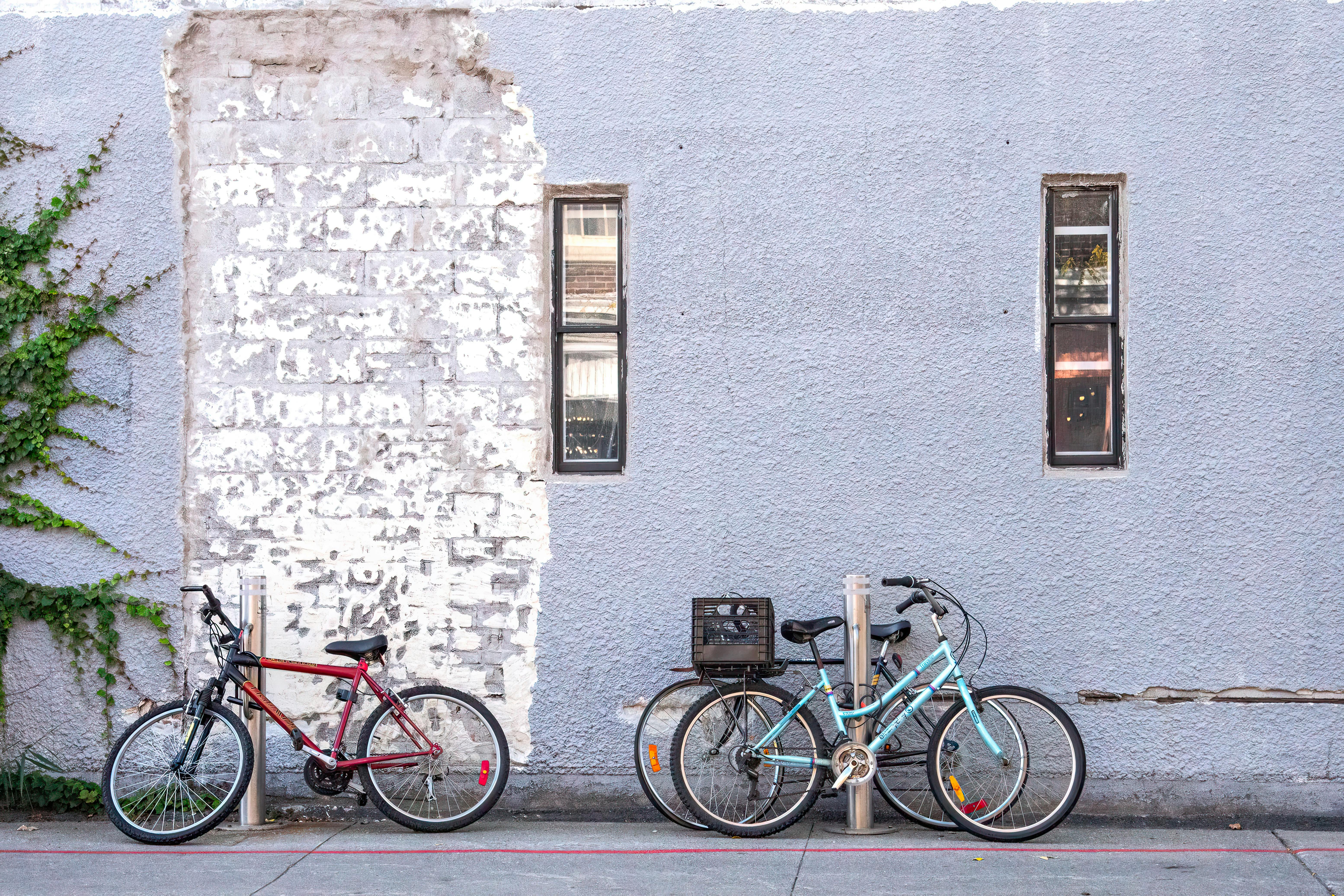Δωρεάν Δύο ποδήλατα ακουμπούν σε έναν ανάγλυφο, μερικώς βαμμένο τοίχο από τούβλα μια ηλιόλουστη μέρα, αποτυπώνοντας την αστική γοητεία. Φωτογραφία από στοκ φωτογραφιών