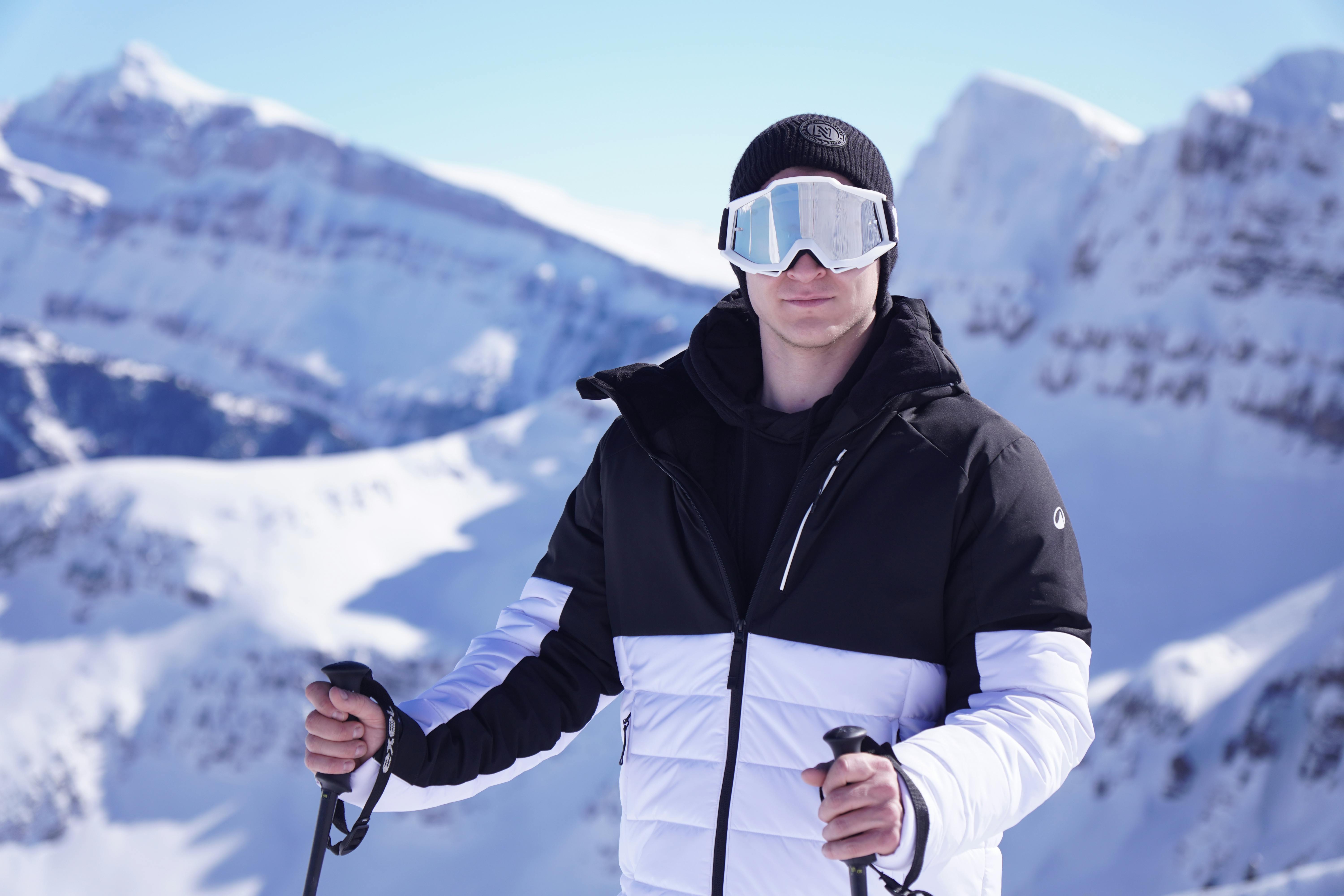 Kostenlos Ein lächelnder junger Skifahrer genießt mit seinen Skistöcken einen sonnigen Tag auf schneebedeckten Berghängen. Stock-Foto