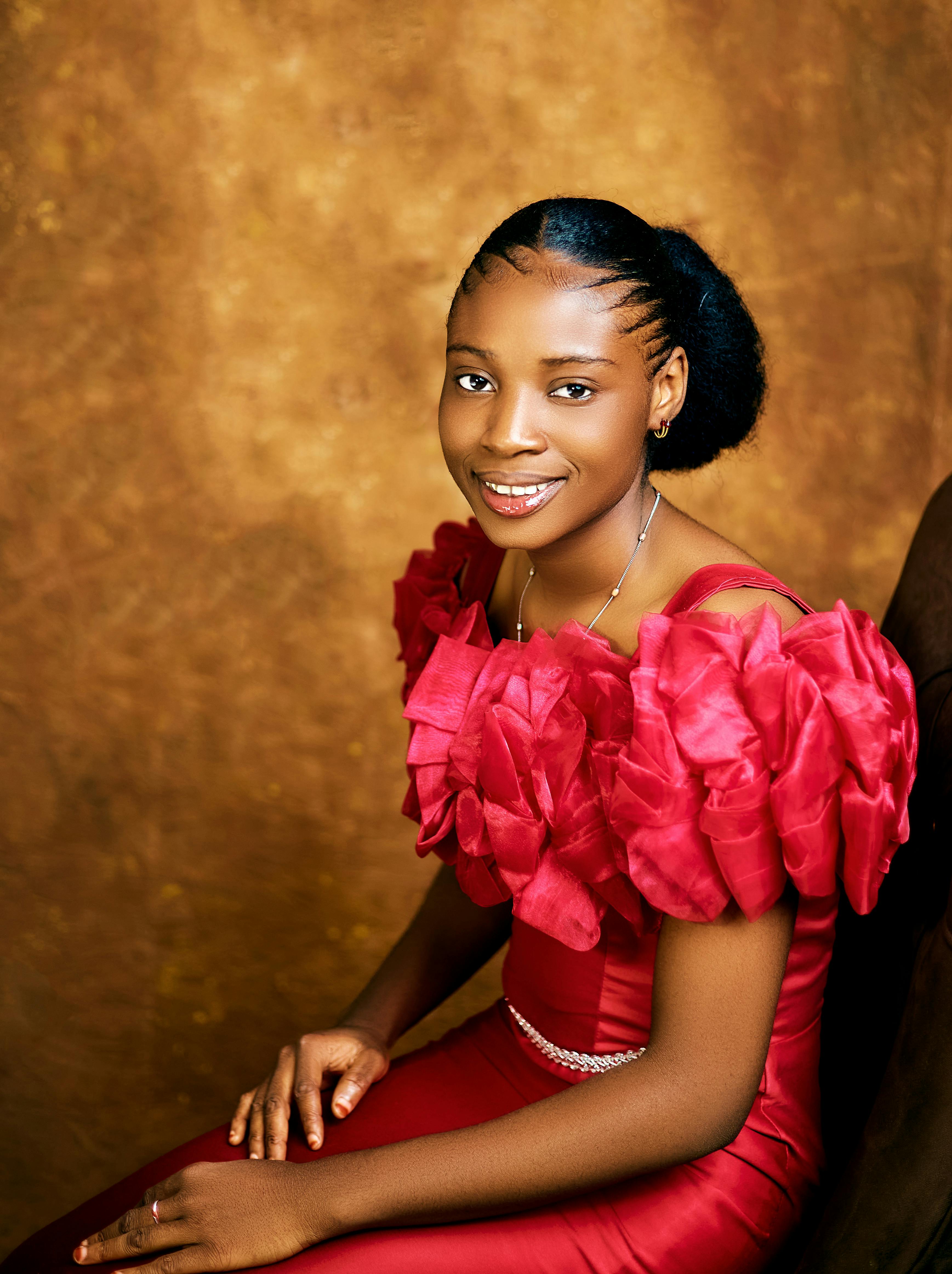 Gratis En grasiøs kvinne i en rød kjole som sitter mot en teksturert bakgrunn og utstråler eleganse. Arkivbilde