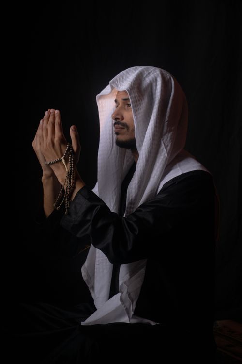 Free A man in traditional Middle Eastern attire prays with a rosary against a dark backdrop. Stock Photo