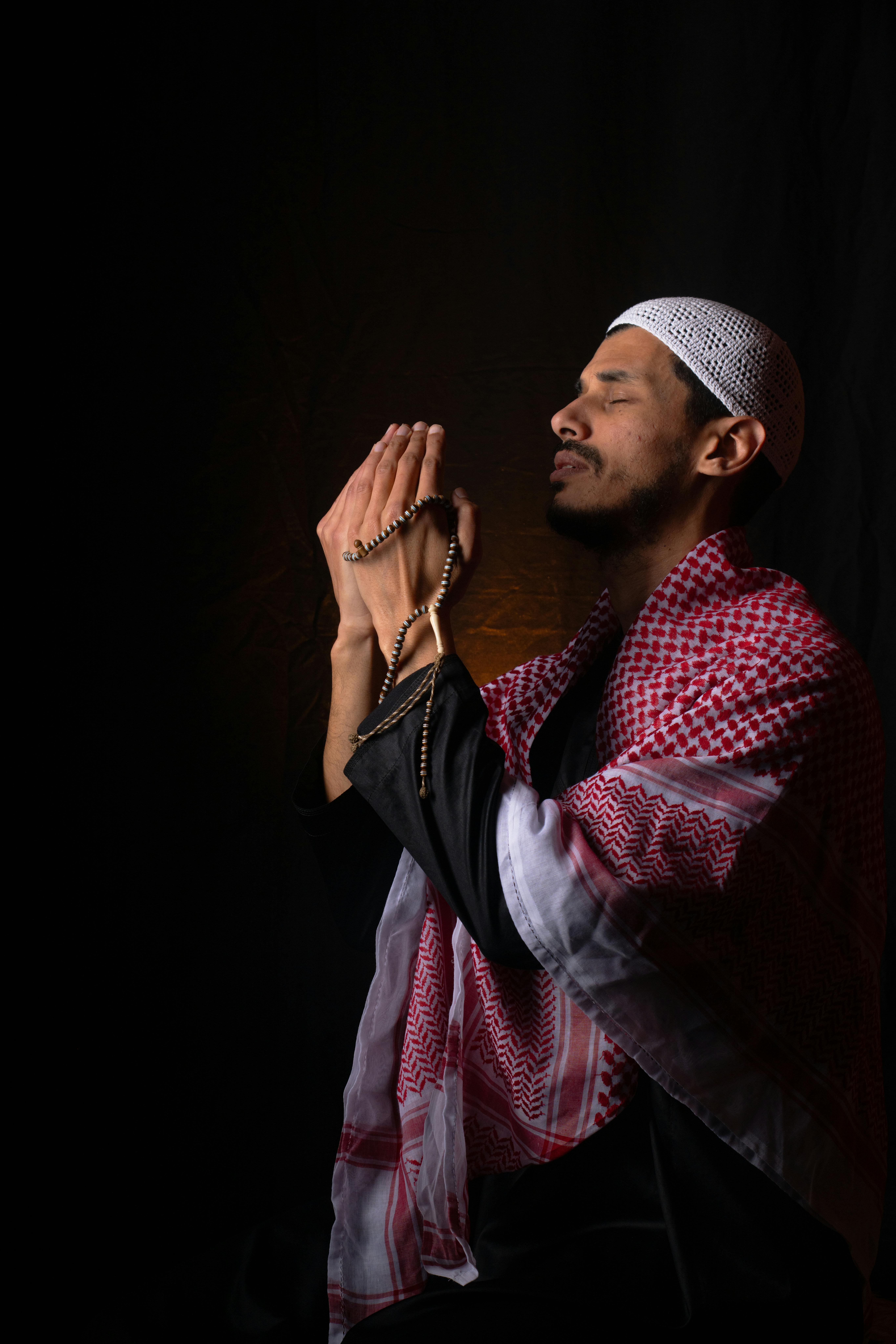 Kostenlos Ein Mann in traditioneller Kleidung aus dem Nahen Osten betet in dunkler Umgebung mit einem Gebetskranz. Stock-Foto