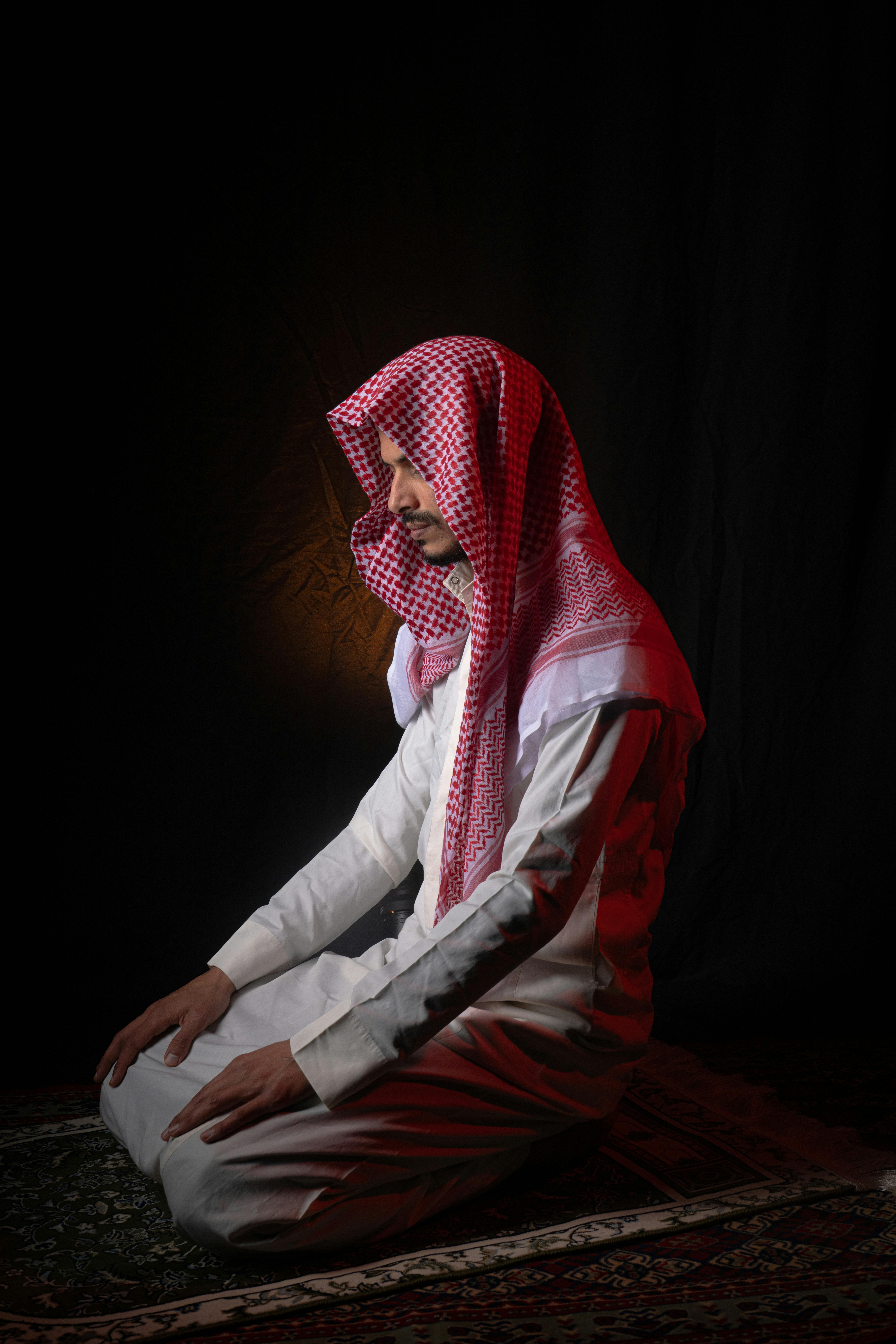 Kostenlos Ein Mann aus dem Nahen Osten in traditioneller Kleidung betet friedlich in einem sanft beleuchteten Raum. Stock-Foto