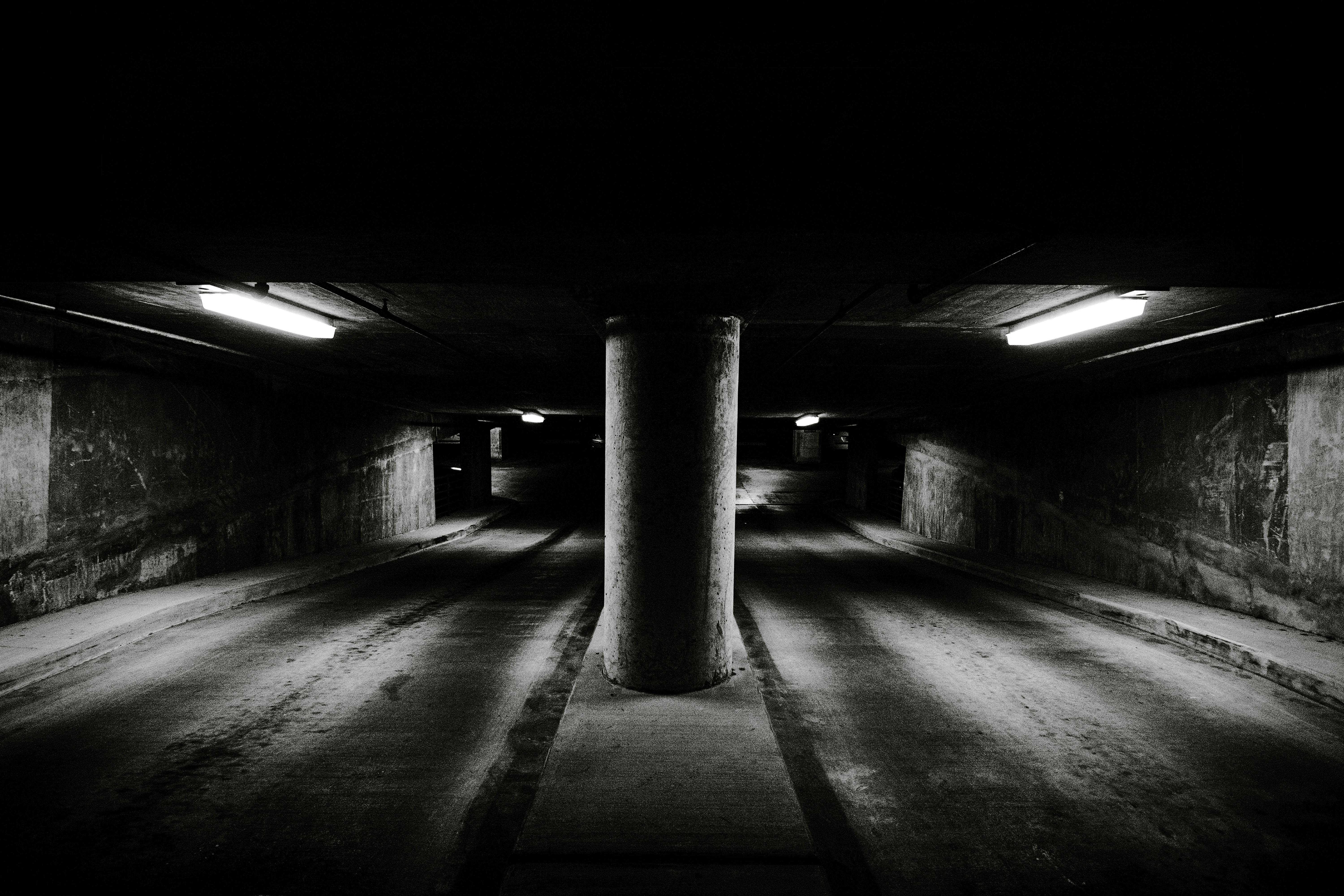 Δωρεάν Ζοφερή ασπρόμαυρη εικόνα ενός υπόγειου γκαράζ στάθμευσης με κεντρική τσιμεντένια κολόνα και εντυπωσιακό φωτισμό. Φωτογραφία από στοκ φωτογραφιών