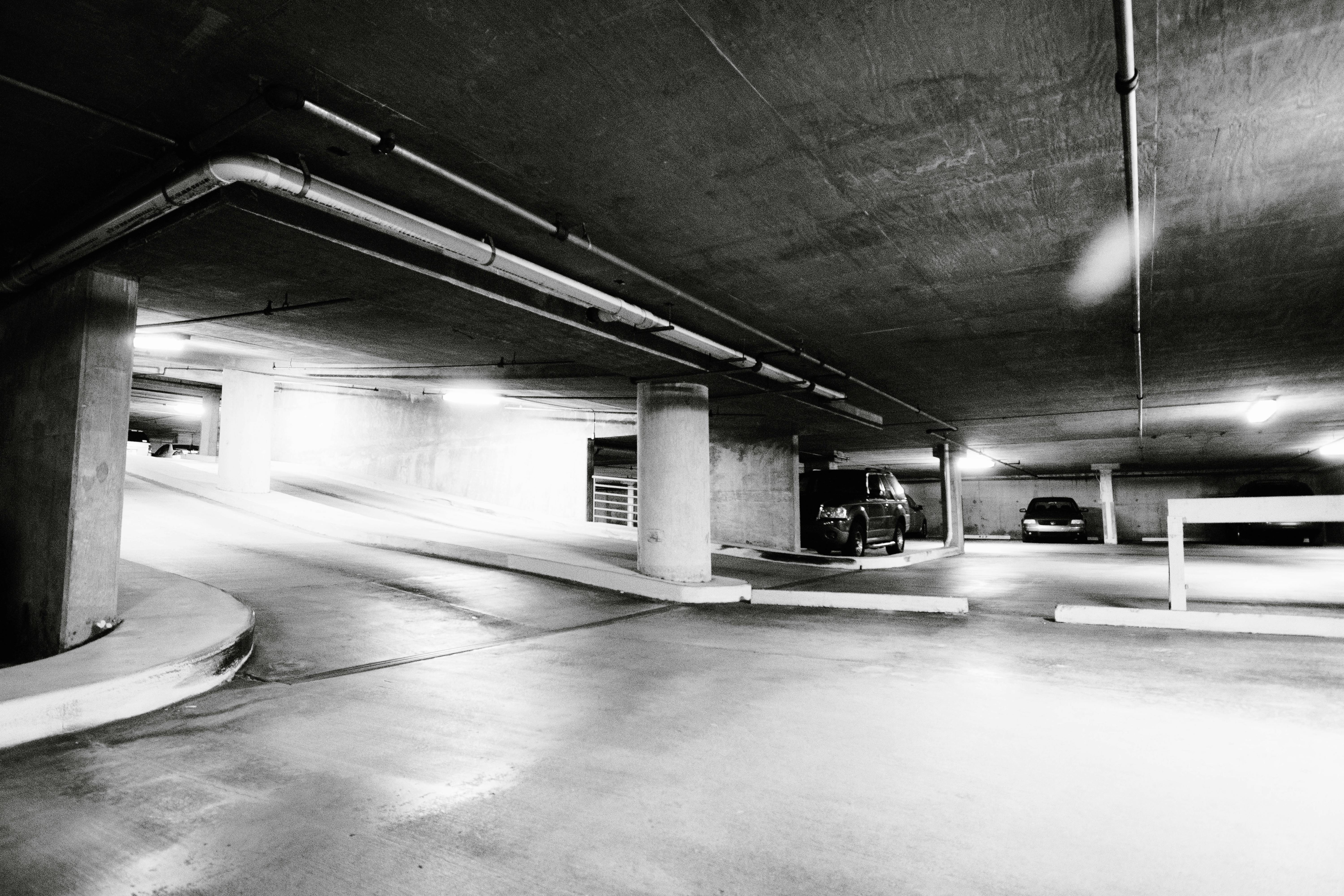 無料 駐車された車とコンクリートの柱がある広々とした地下駐車場の白黒写真。 写真素材