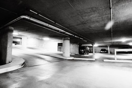 Free Black and white photo of a spacious underground parking garage with cars parked and concrete pillars. Stock Photo