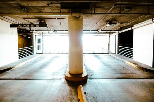 A brightly lit empty parking garage with a central pillar and 'Do Not Enter' sign.