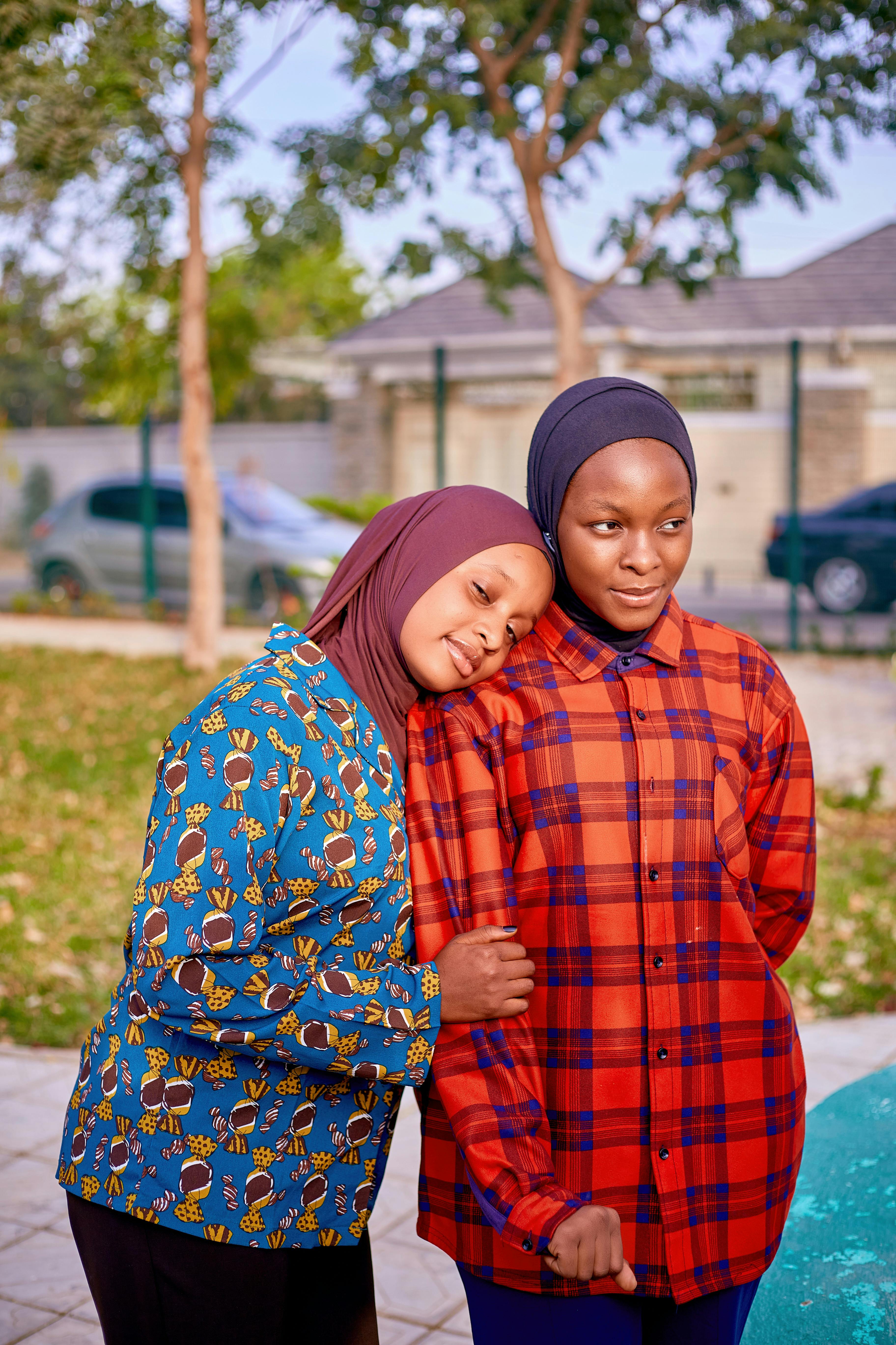Kostenlos Zwei junge Frauen mit farbenfrohen Hijabs lächeln und umarmen sich in einem Park im Freien. Stock-Foto