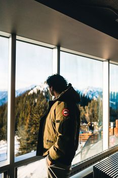 A person looks out a window at the snowy mountains of Banff National Park, Alberta, Canada, in winter.