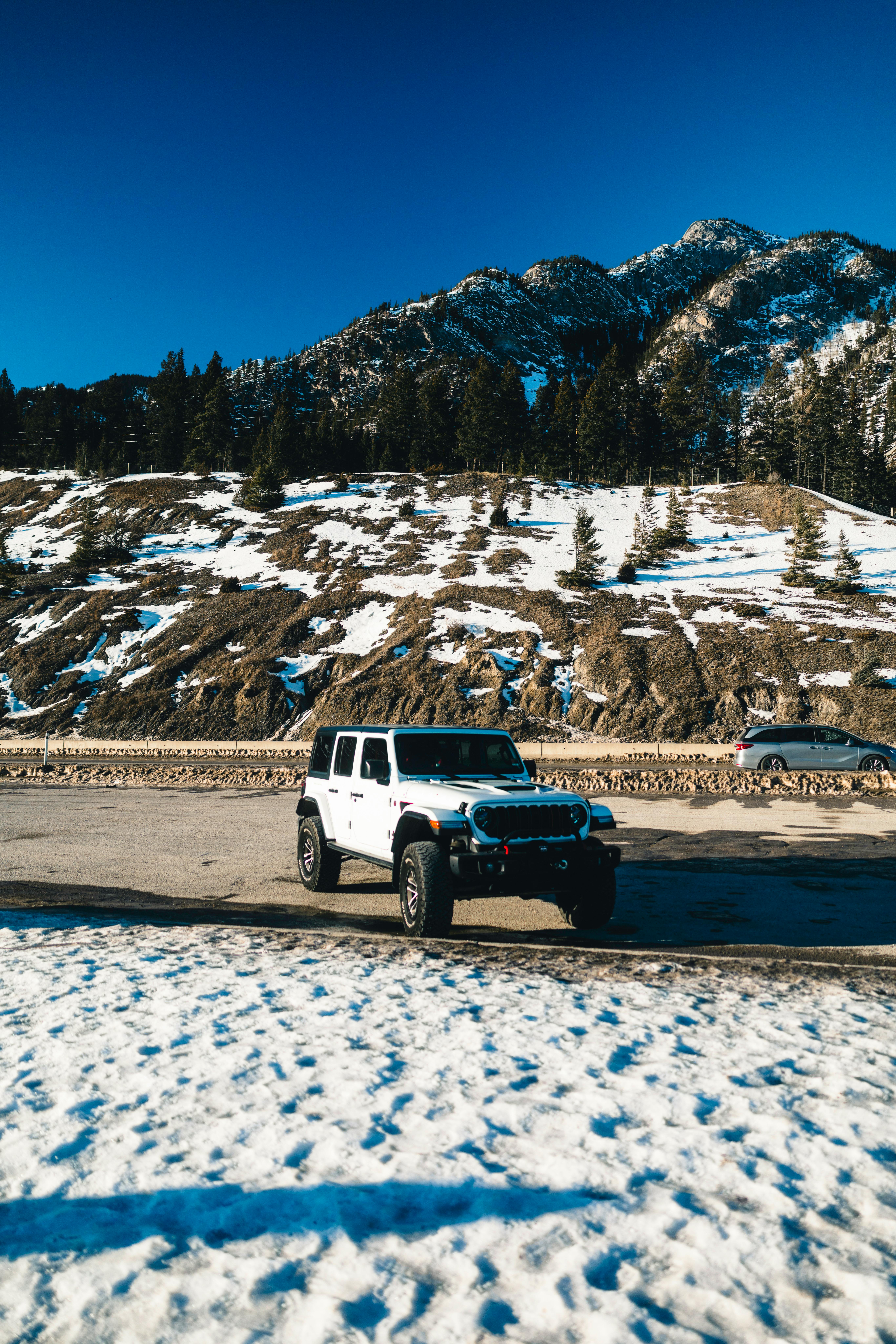 Gratuit Un jeep alb parcat pe teren înzăpezit pe fundalul munților maiestuoși din Banff, sub un cer albastru senin. Fotografie de stoc