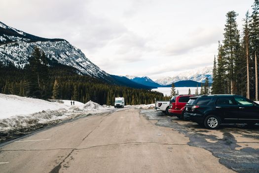 Snowy mountain scenery in Banff, Alberta with cars parked along the roadside.