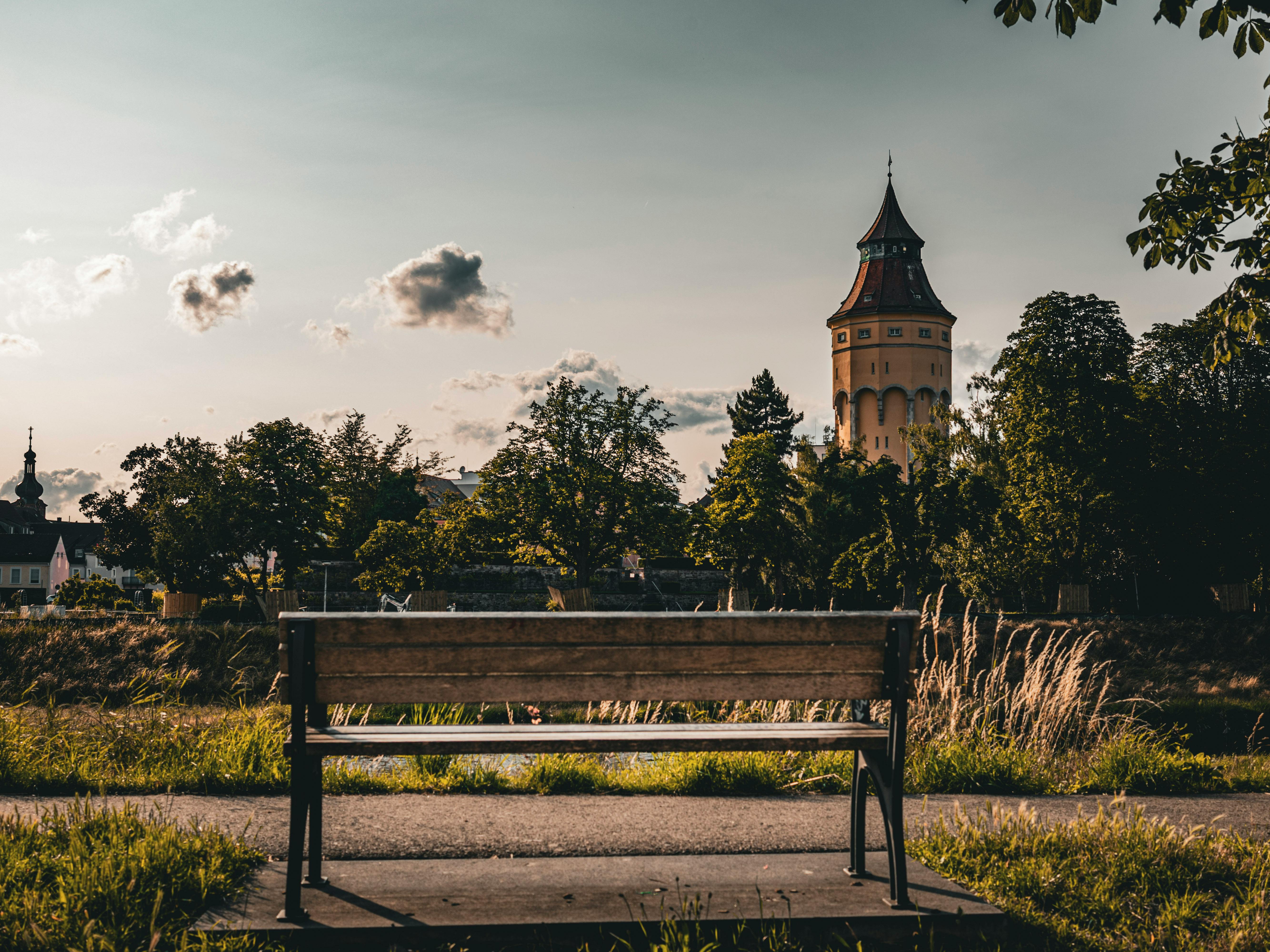 бесплатная Спокойный пейзаж со скамейкой, с которой открывается живописный вид, и характерной башней под облачным небом. Стоковое фото