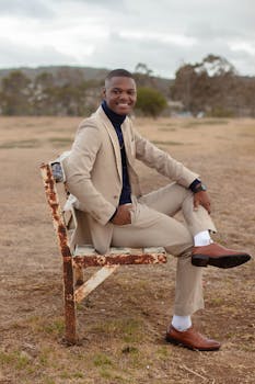 一位穿着正装的时尚年轻人，正坐在户外宁静环境中的长凳上