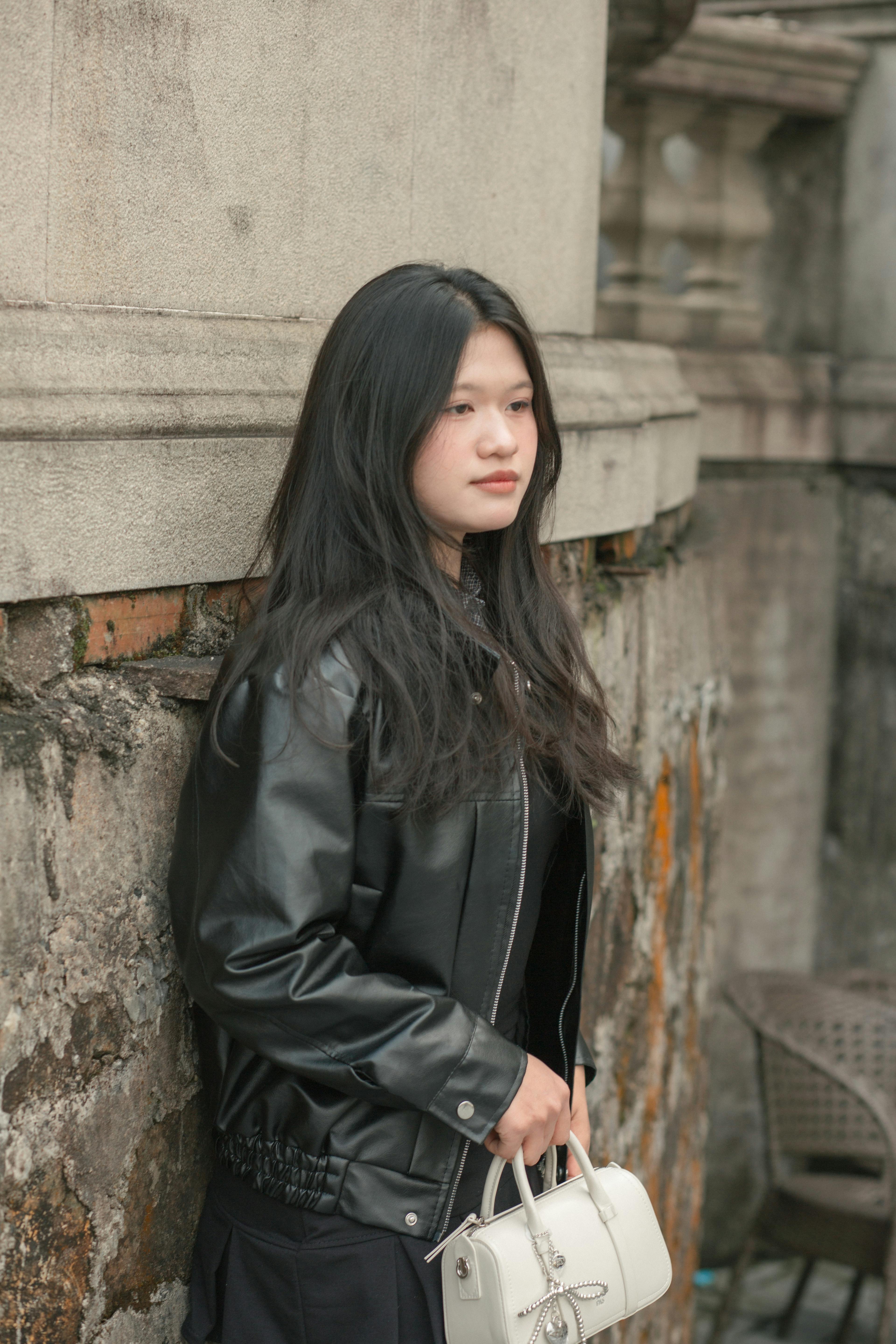 Gratis Stilig ung kvinne med veske står ved en teksturert vegg, et symbol på urban mote. Arkivbilde