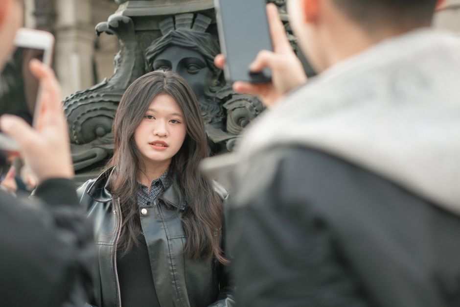 スタイリッシュな若い女性が屋外でポーズを取り、スマートフォンでその光景を撮影しています。