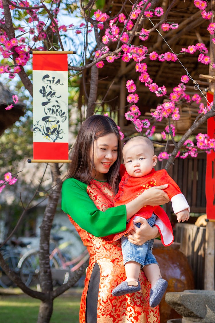 Woman In Red Long Sleeve Shirt Carrying Baby In Red And White Floral Dress