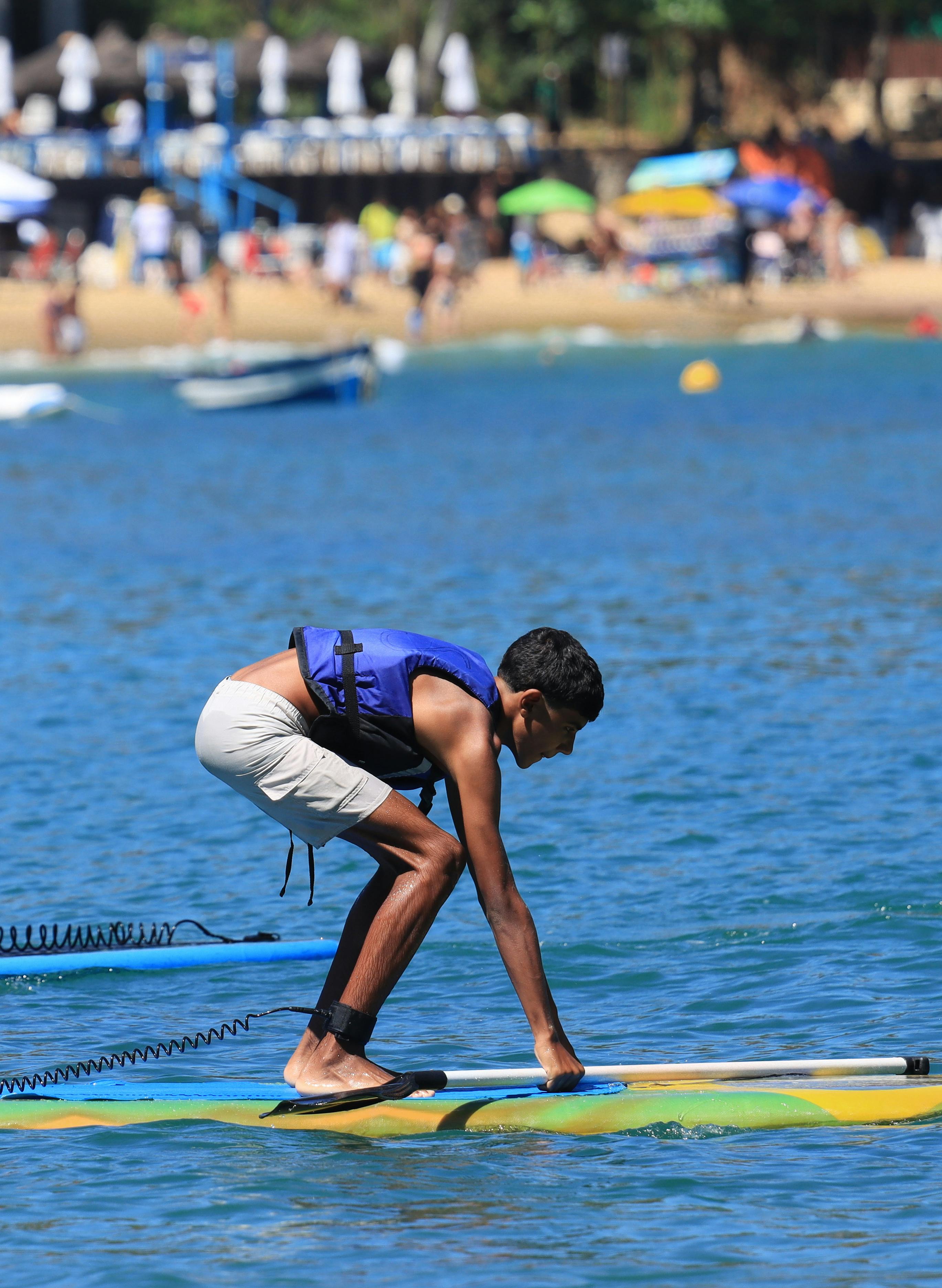 Kostenlos Ein Teenager übt Stand-Up-Paddling an einem sonnigen Strand mit einer lebendigen Küstenlinie. Stock-Foto