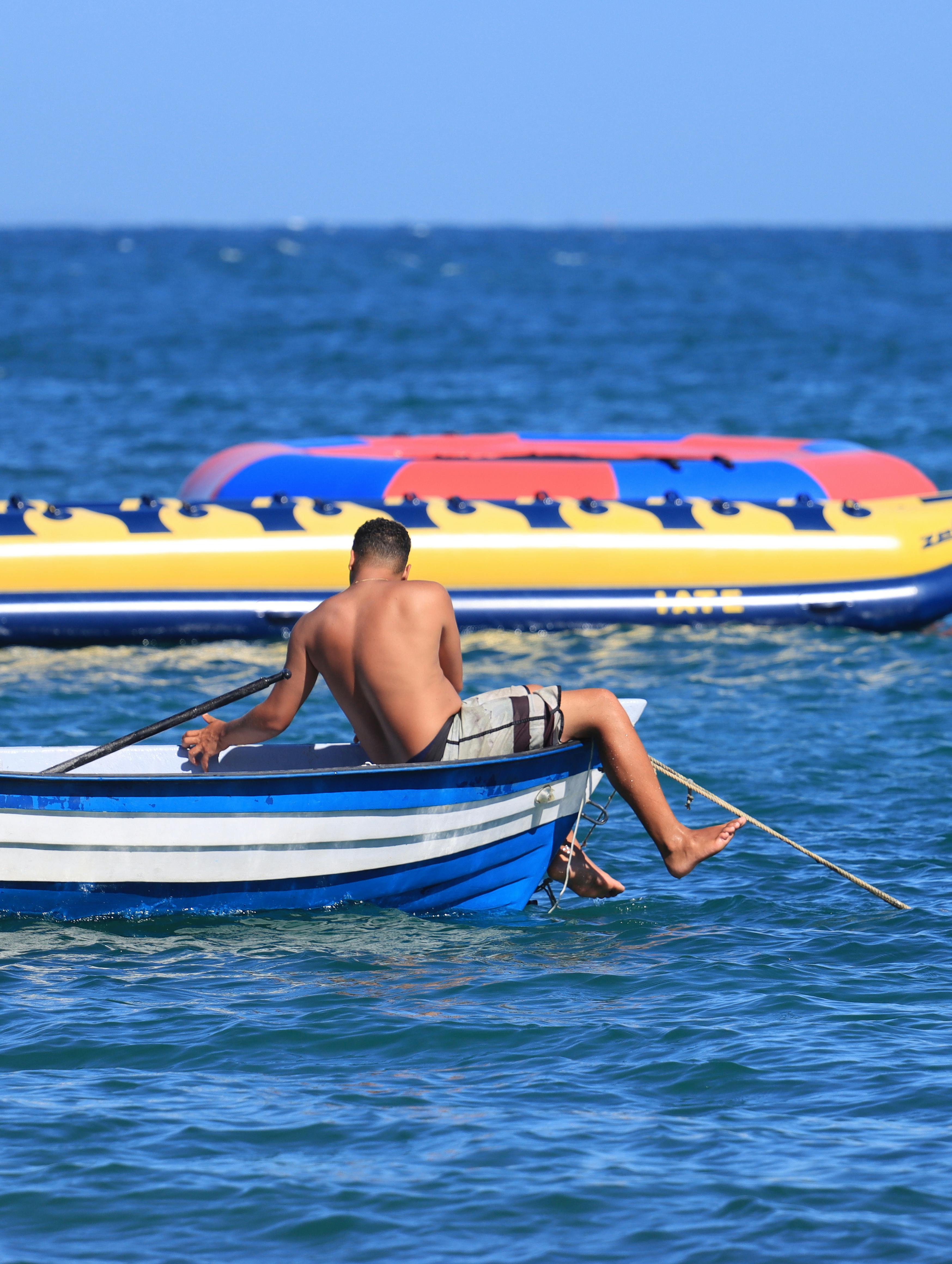 Gratis Mand nyder fritiden i en robåd på havet med en oppustelig tur i baggrunden. Lagerfoto