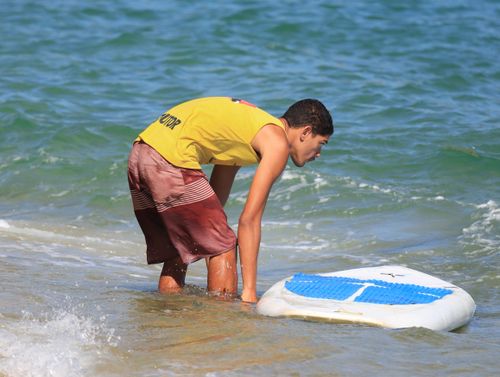 Free Young male setting up paddleboard at sunny beach, enjoying outdoor summer activity. Stock Photo