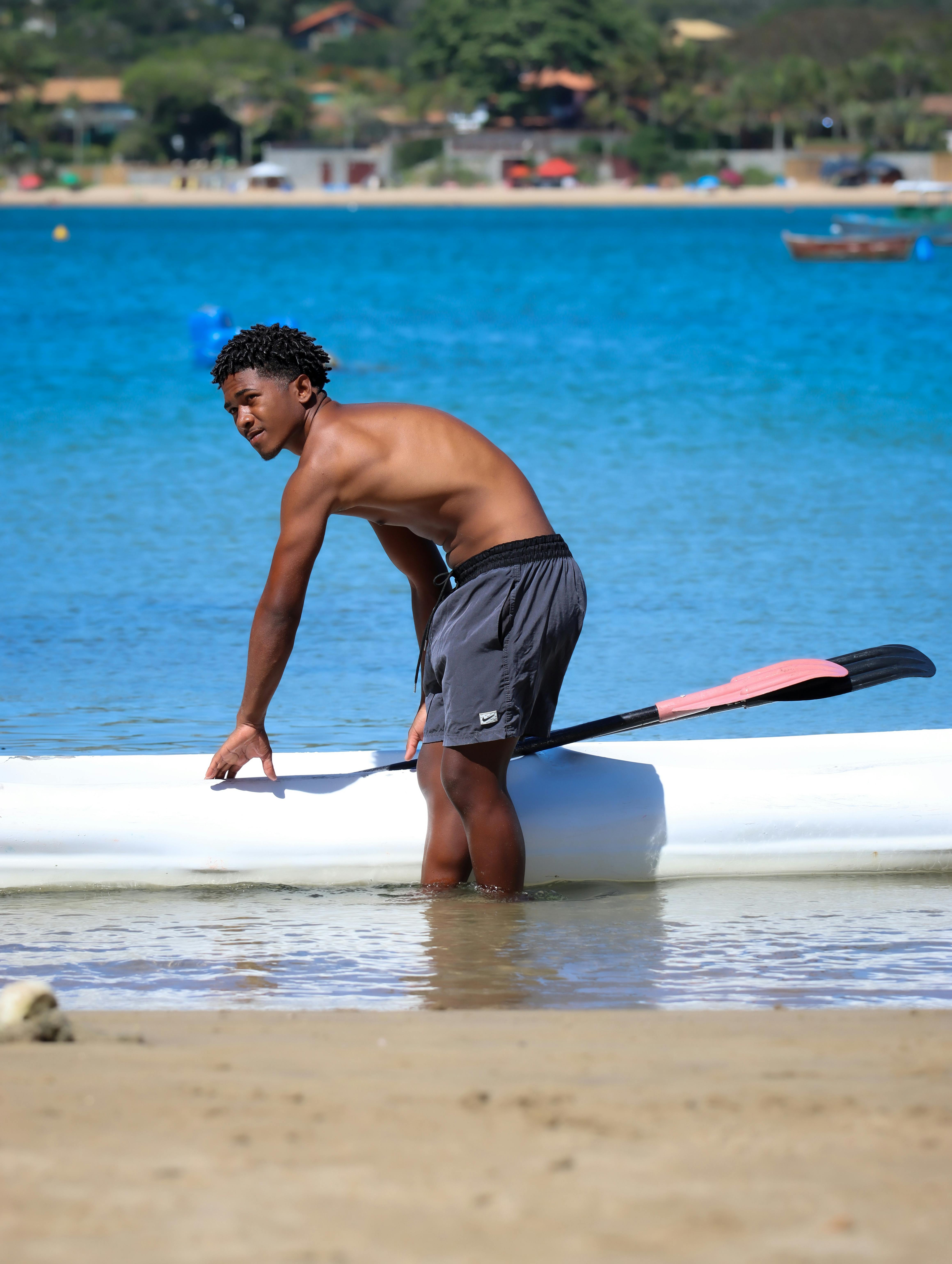 Gratis En ung mand står ved sin kajak på en solrig strand og forbereder sig på en dag i kajak. Lagerfoto