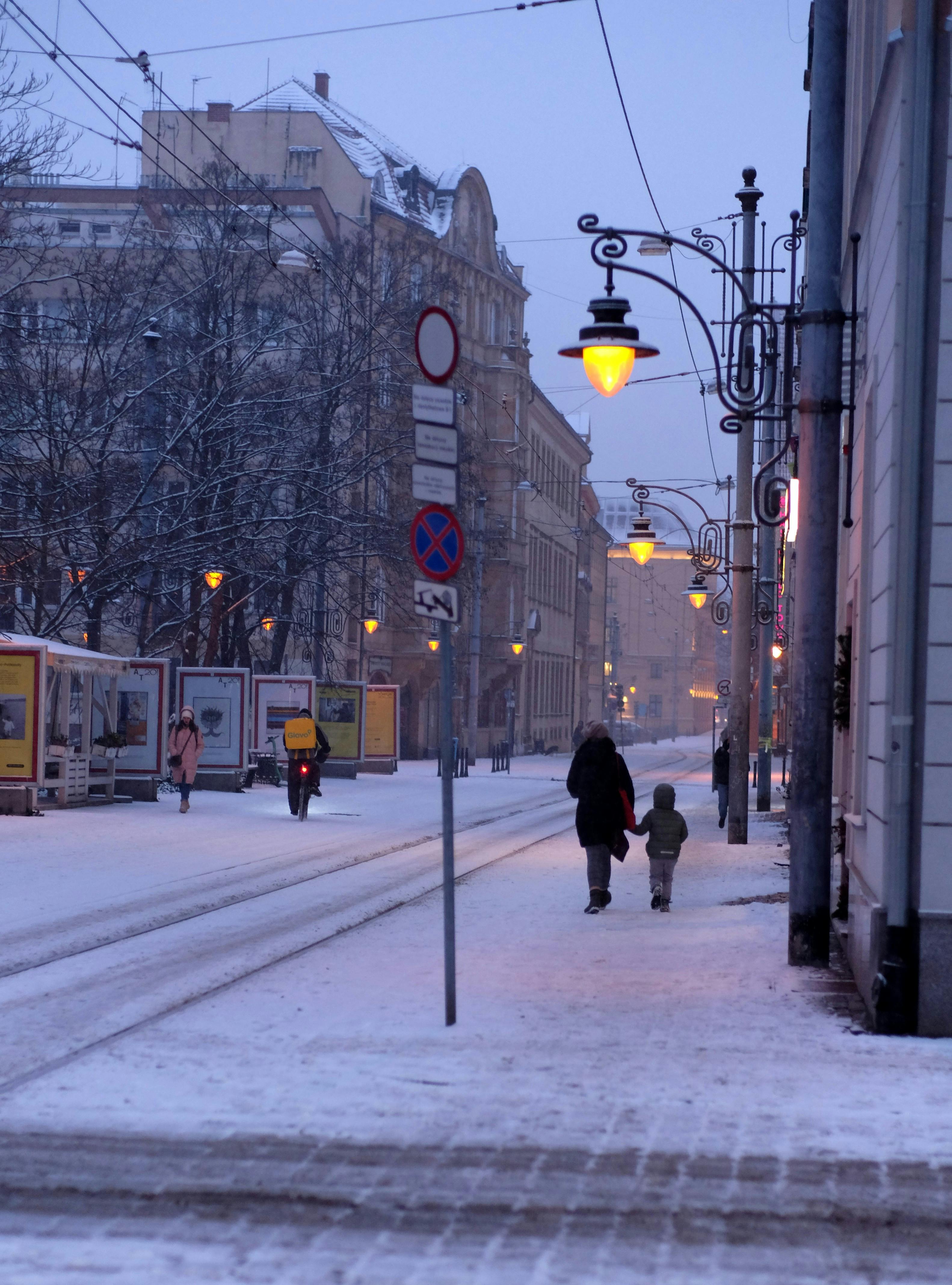Δωρεάν Ένα γαλήνιο χειμωνιάτικο βράδυ σε έναν χιονισμένο δρόμο της πόλης με ανθρώπους να περπατούν κάτω από τα φώτα του δρόμου. Φωτογραφία από στοκ φωτογραφιών