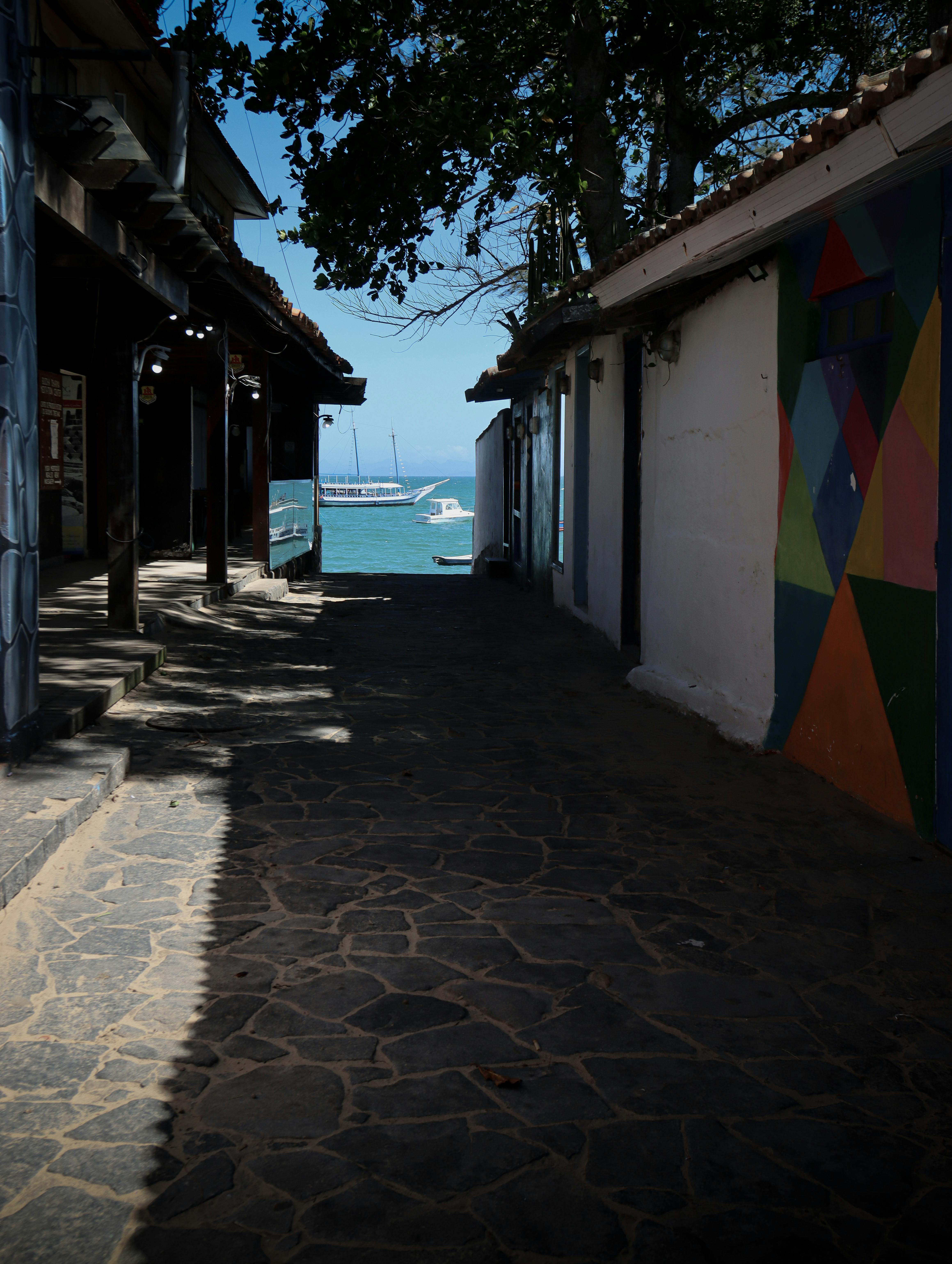 Δωρεάν Ανακαλύψτε ένα ήσυχο παραθαλάσσιο σοκάκι που οδηγεί σε μια γραφική θέα στη θάλασσα, με ζωντανές τοιχογραφίες. Φωτογραφία από στοκ φωτογραφιών