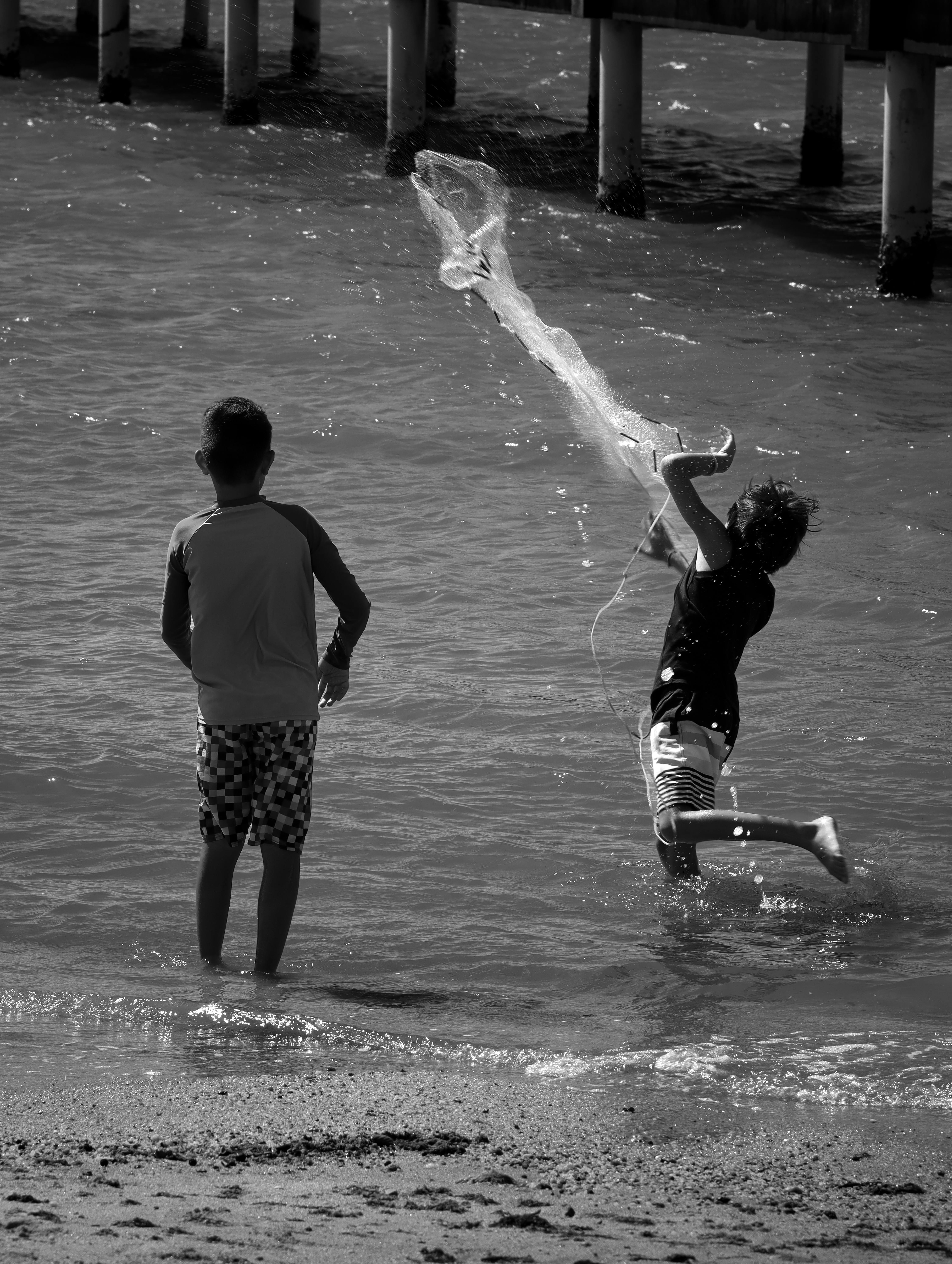 Kostenlos Zwei Kinder haben Spaß am Angeln am Strand und werfen ein Netz ins Meer. Stock-Foto