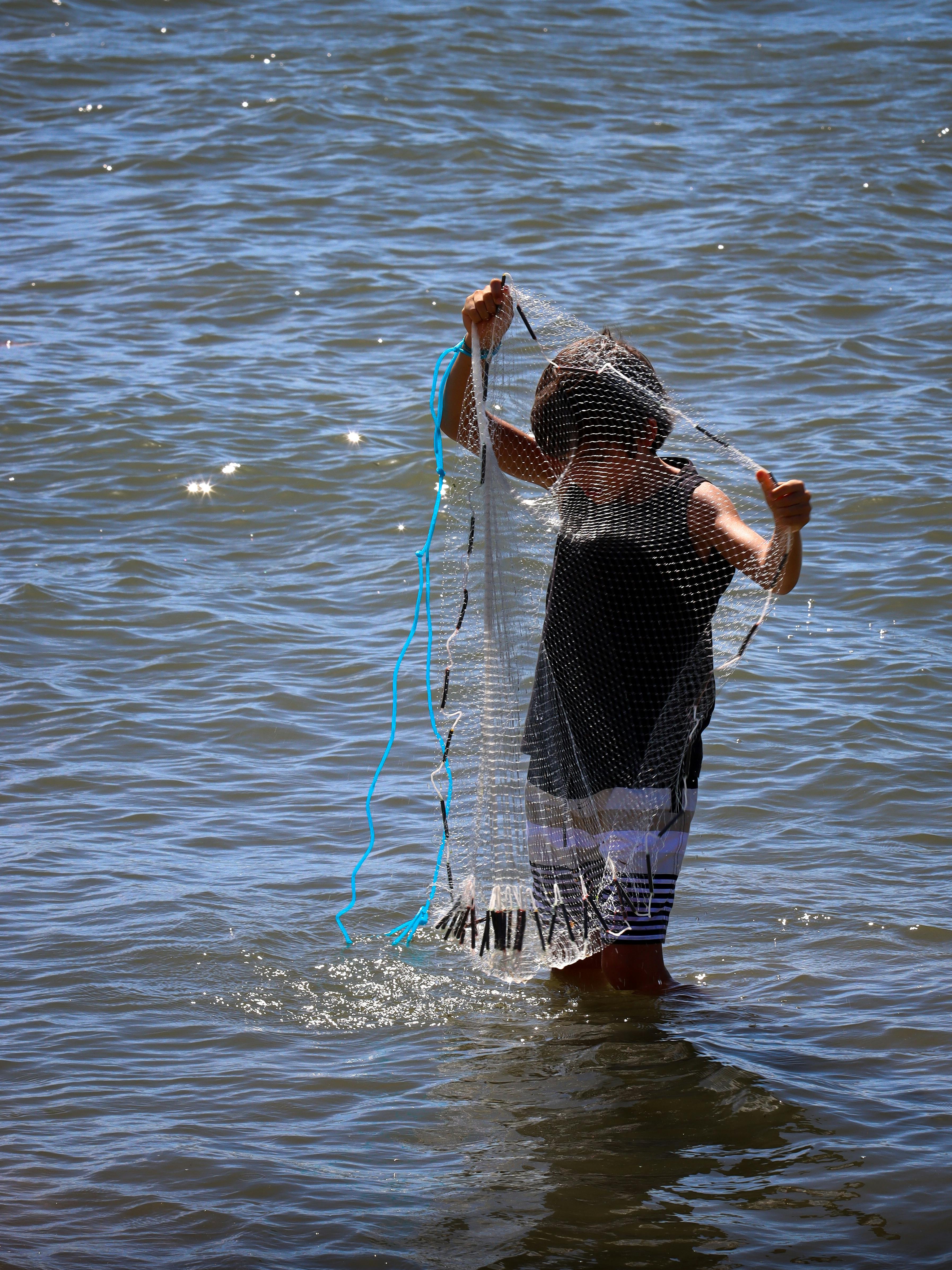 Kostenlos Ein Kind fängt an einem sonnigen Tag in einem ruhigen Fluss mit einem Netz Fische und unterstreicht damit das Abenteuer in der Natur. Stock-Foto