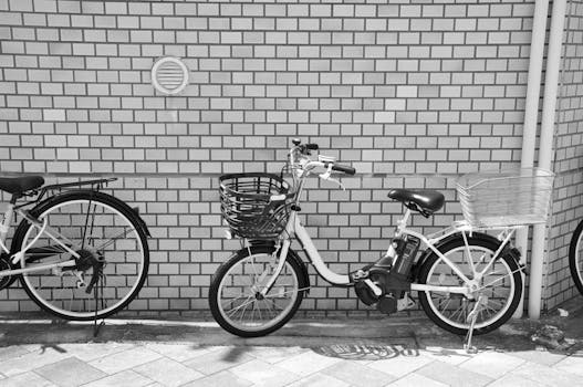 Black and white image of bicycles with baskets against a brick wall outdoors.