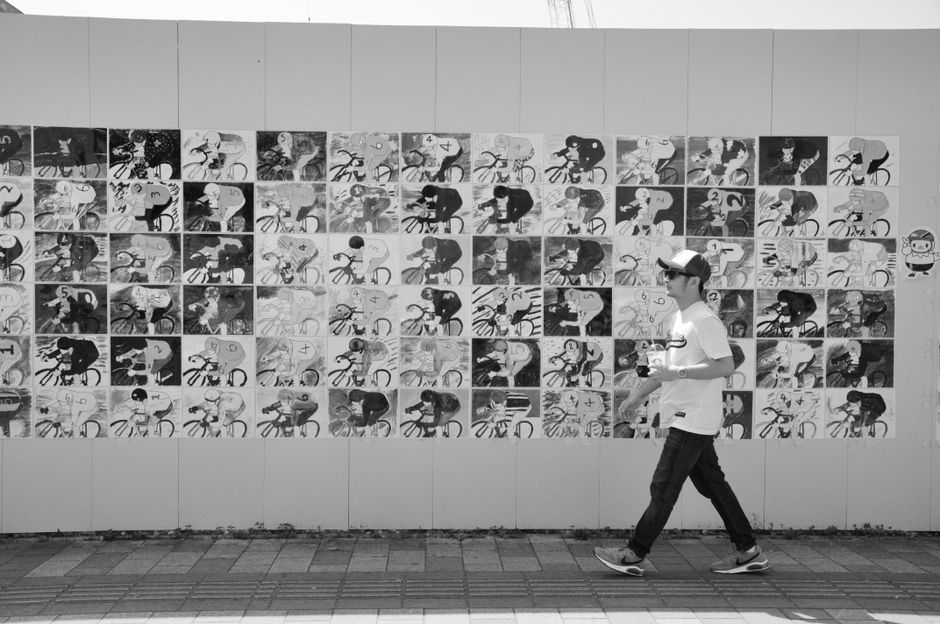 Black and white photo of a man walking past a detailed mural of cyclists.